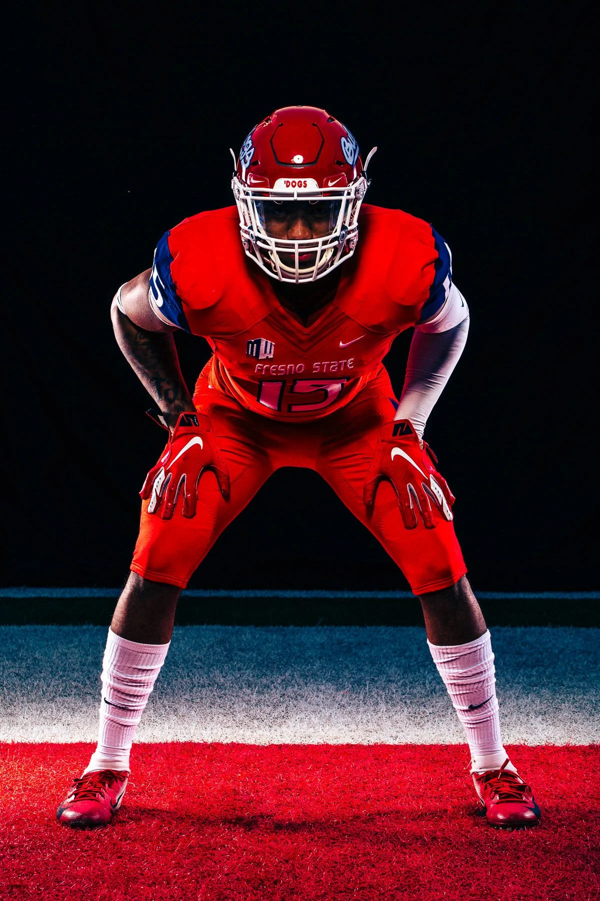 American football player in red Fresno State uniform, crouched in a ready stance on the field, against a dark background.