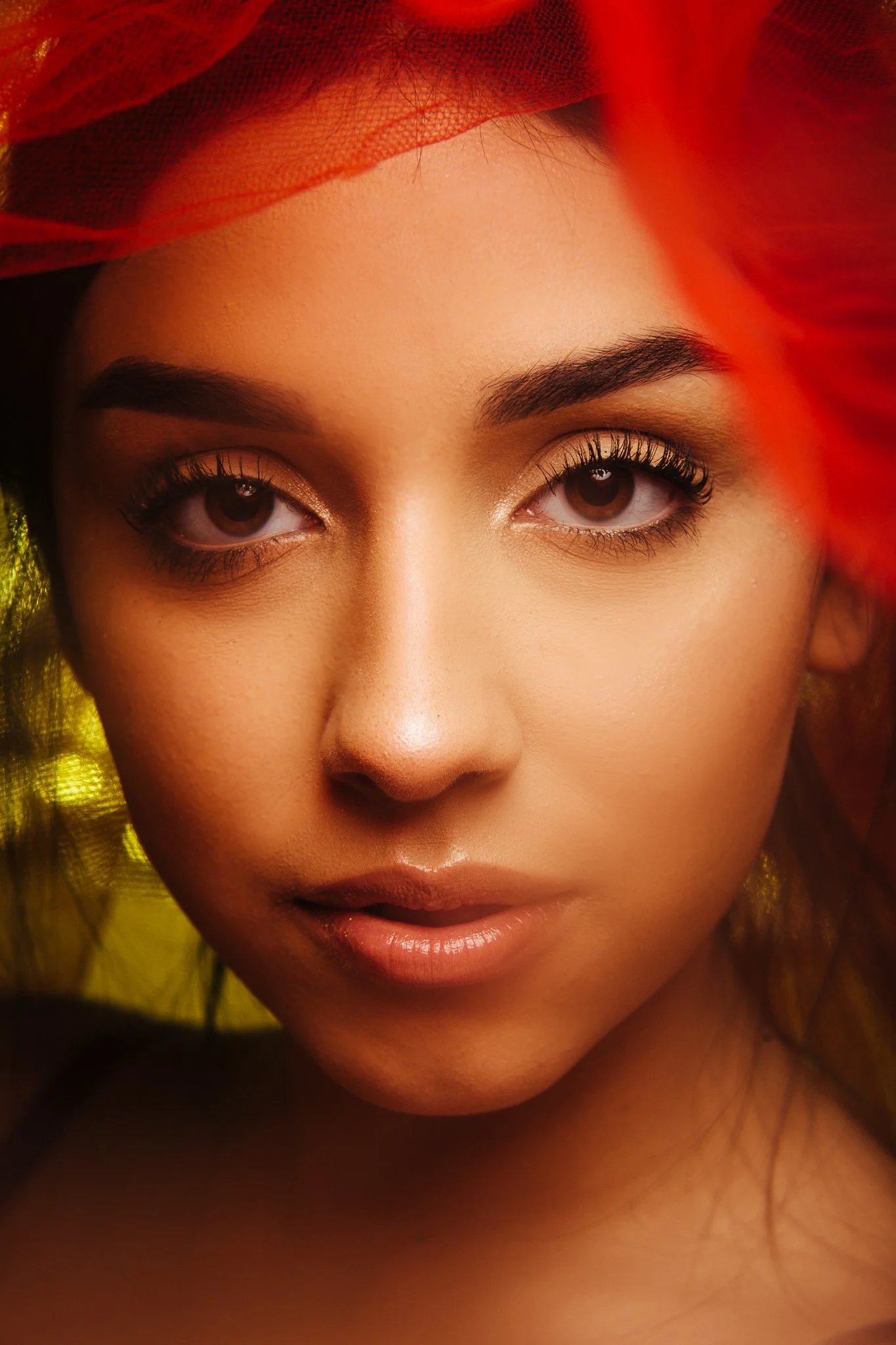 Close-up portrait of a woman with makeup and red fabric in her hair.