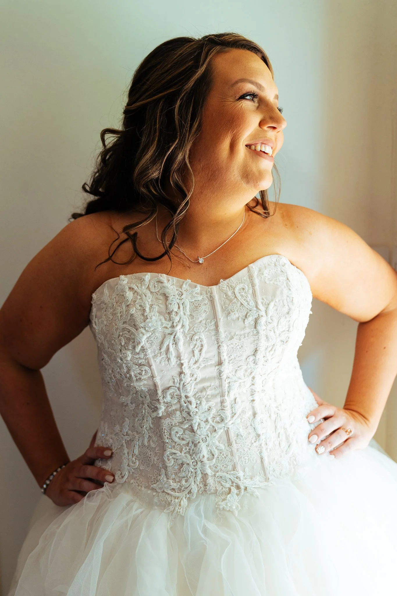 A woman in a wedding dress, smiling and looking out a window.
