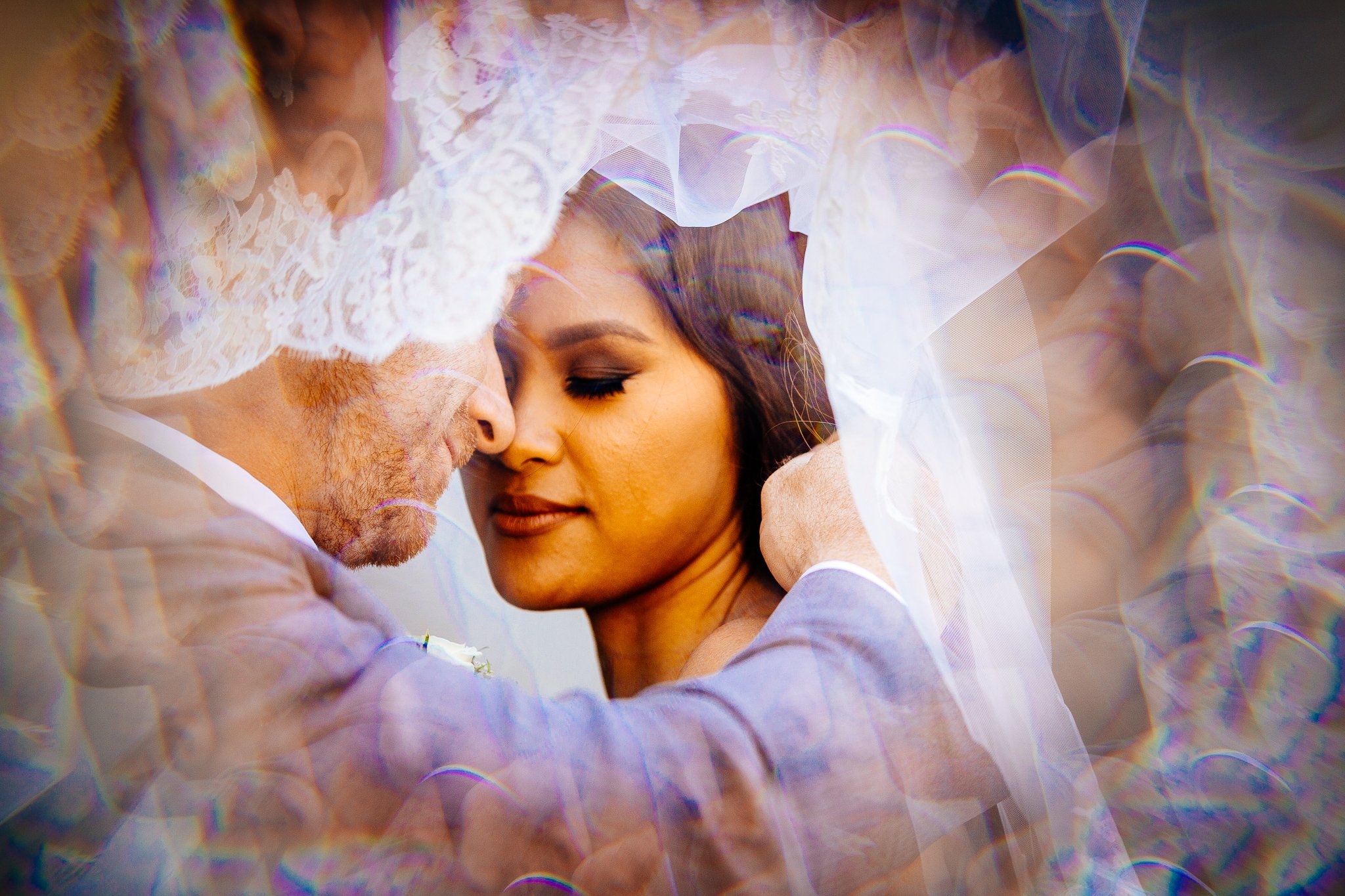 A couple in wedding attire sharing an intimate moment under a lace veil.