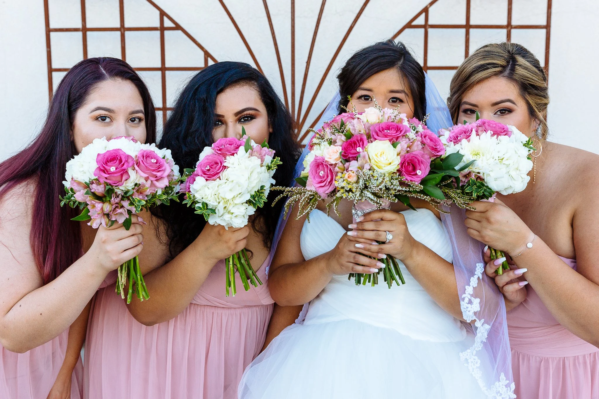 Four women standing close together, each holding a bouquet of pink and white flowers, at a wedding.