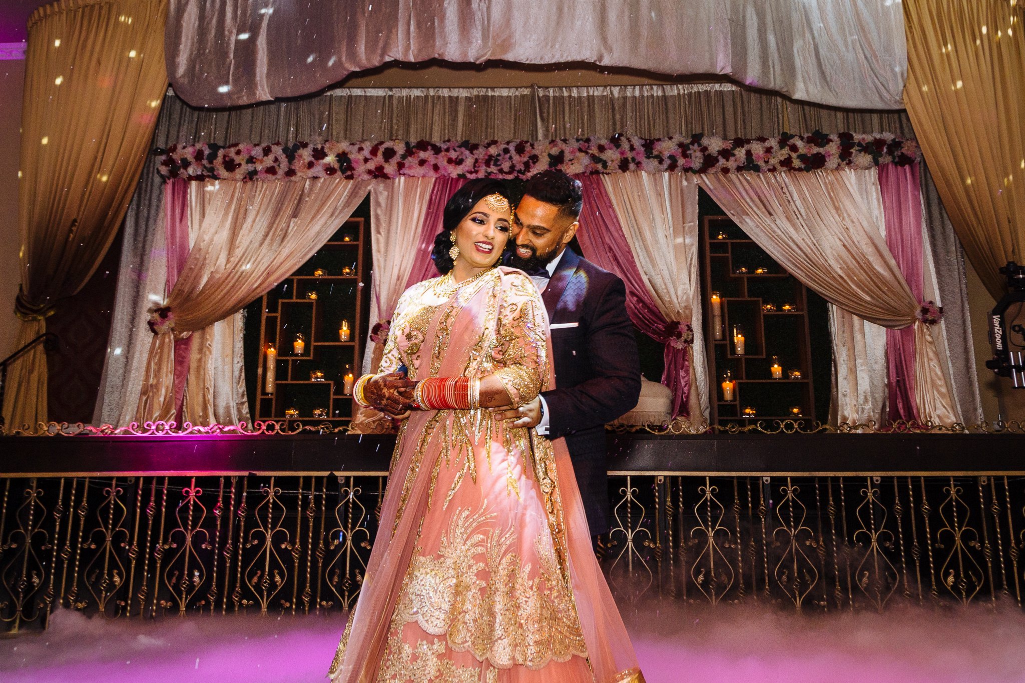 A bride and groom dance together at their wedding reception, with romantic candlelit decor and draped curtains in the background.