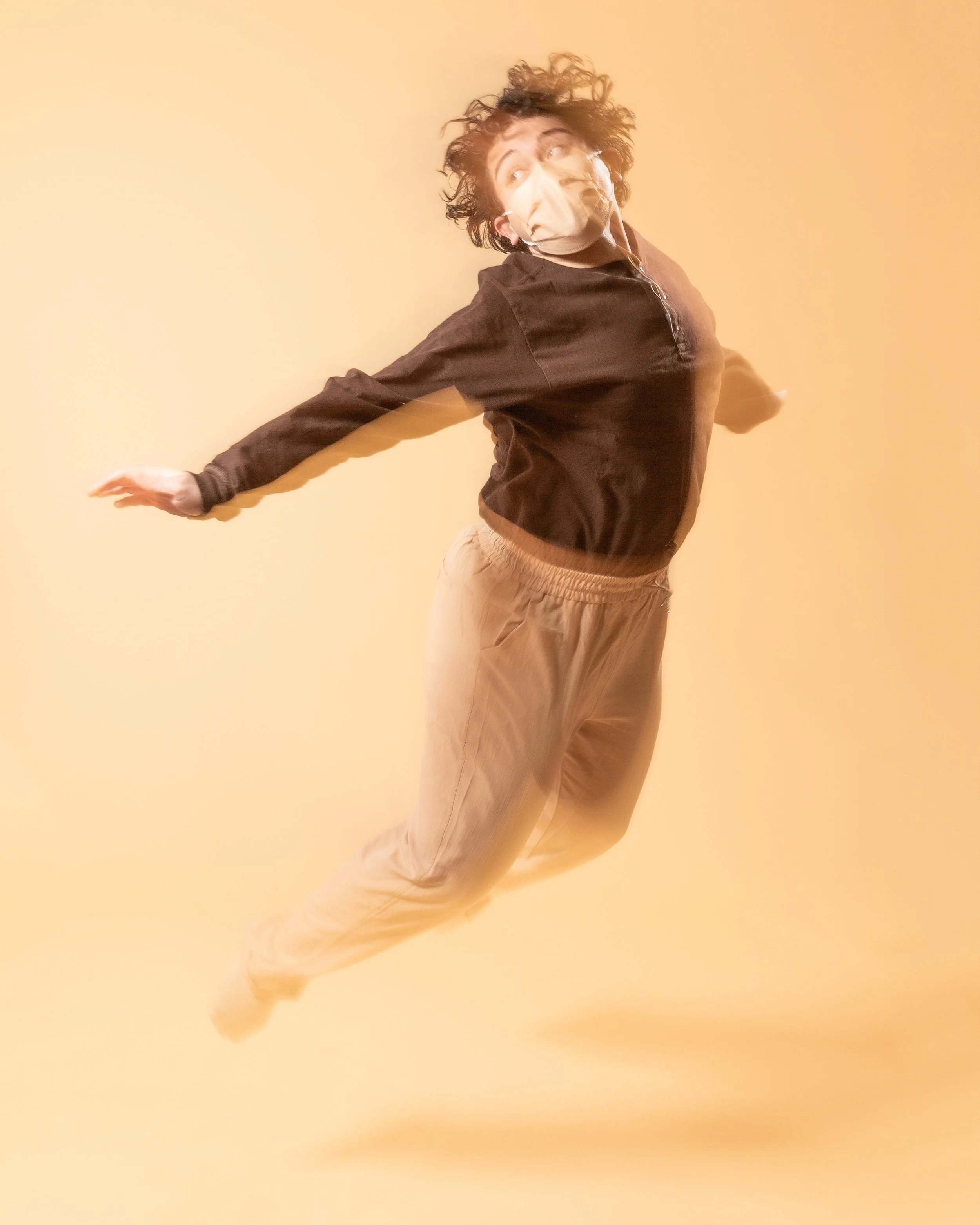 Person in black jacket and beige pants floating or flying in front of a yellow background.
