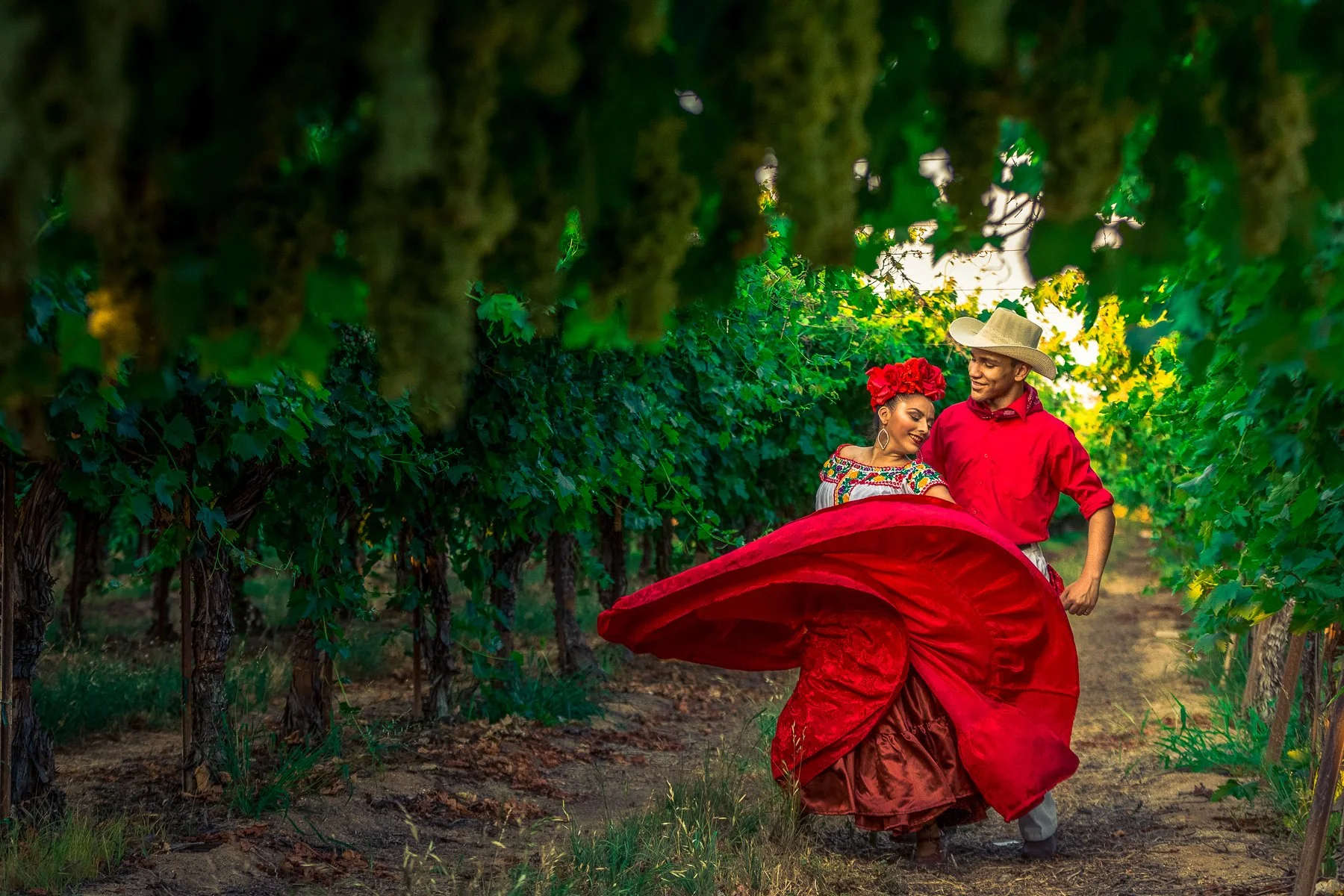 A couple dancing in a vineyard, dressed in traditional Mexican attire, with green vines surrounding them