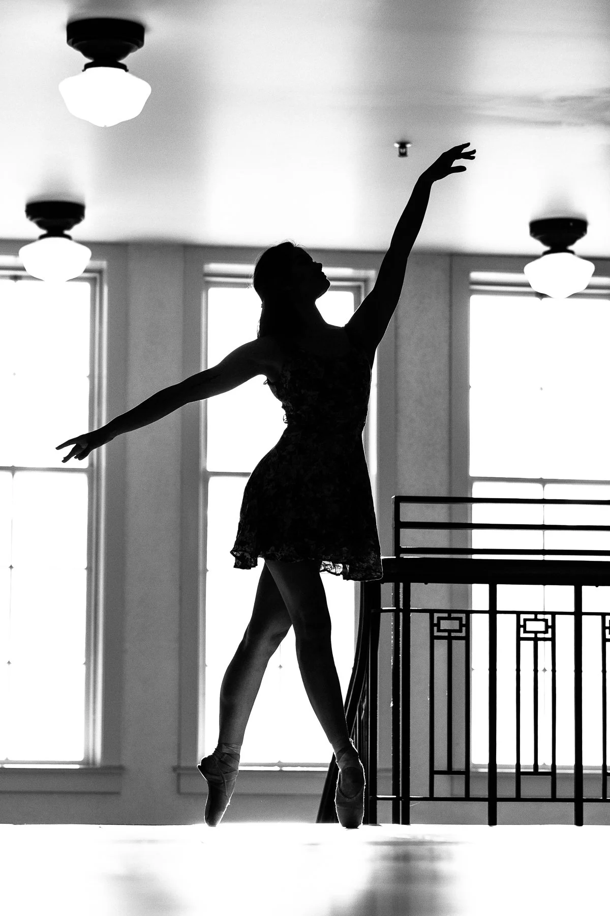 Silhouette of a ballerina dancing on pointe in a studio with large windows and ceiling lights.