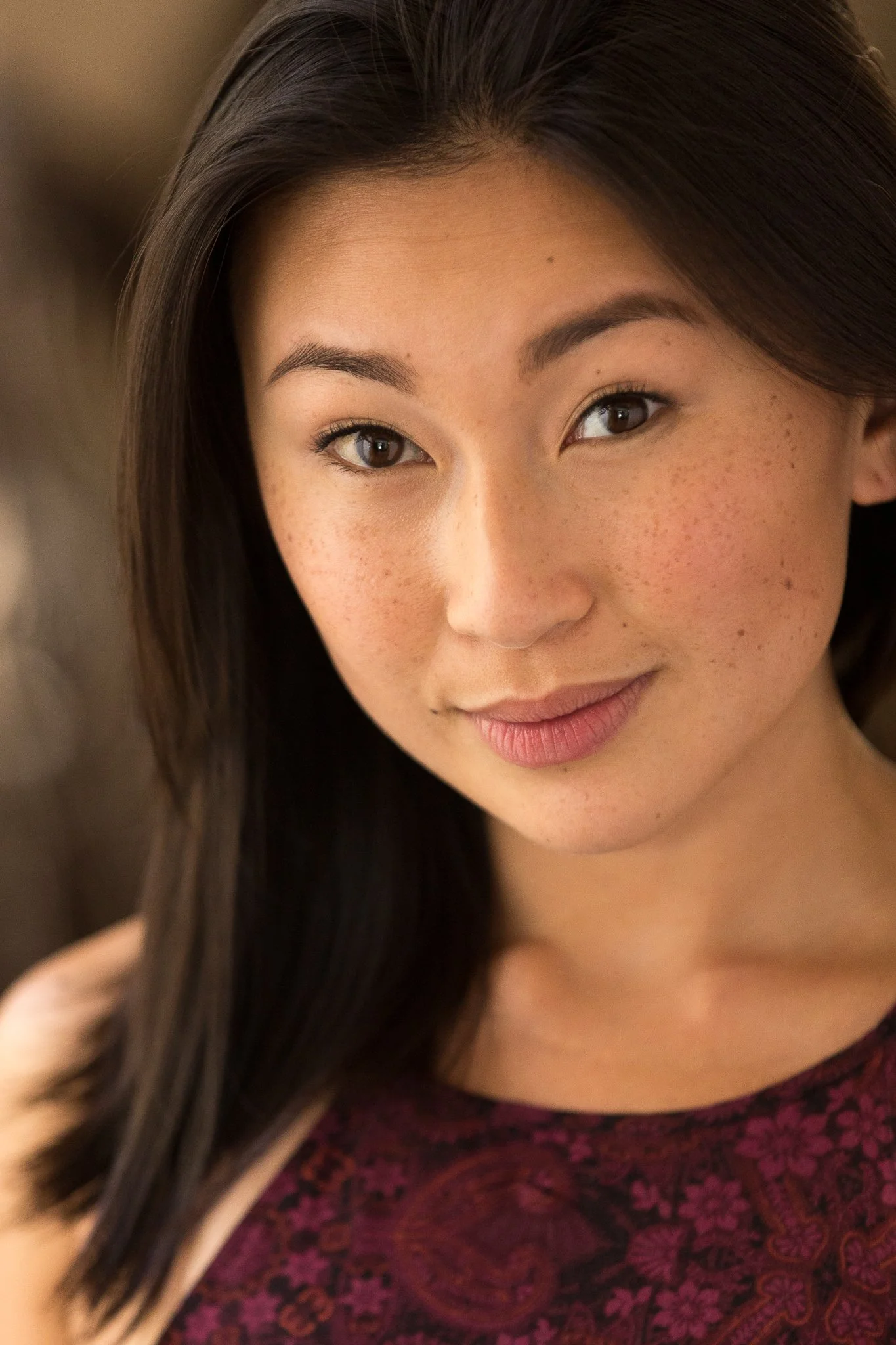 Close-up of a young woman with long dark hair, light brown skin, and freckles, looking at the camera with a slight smile.