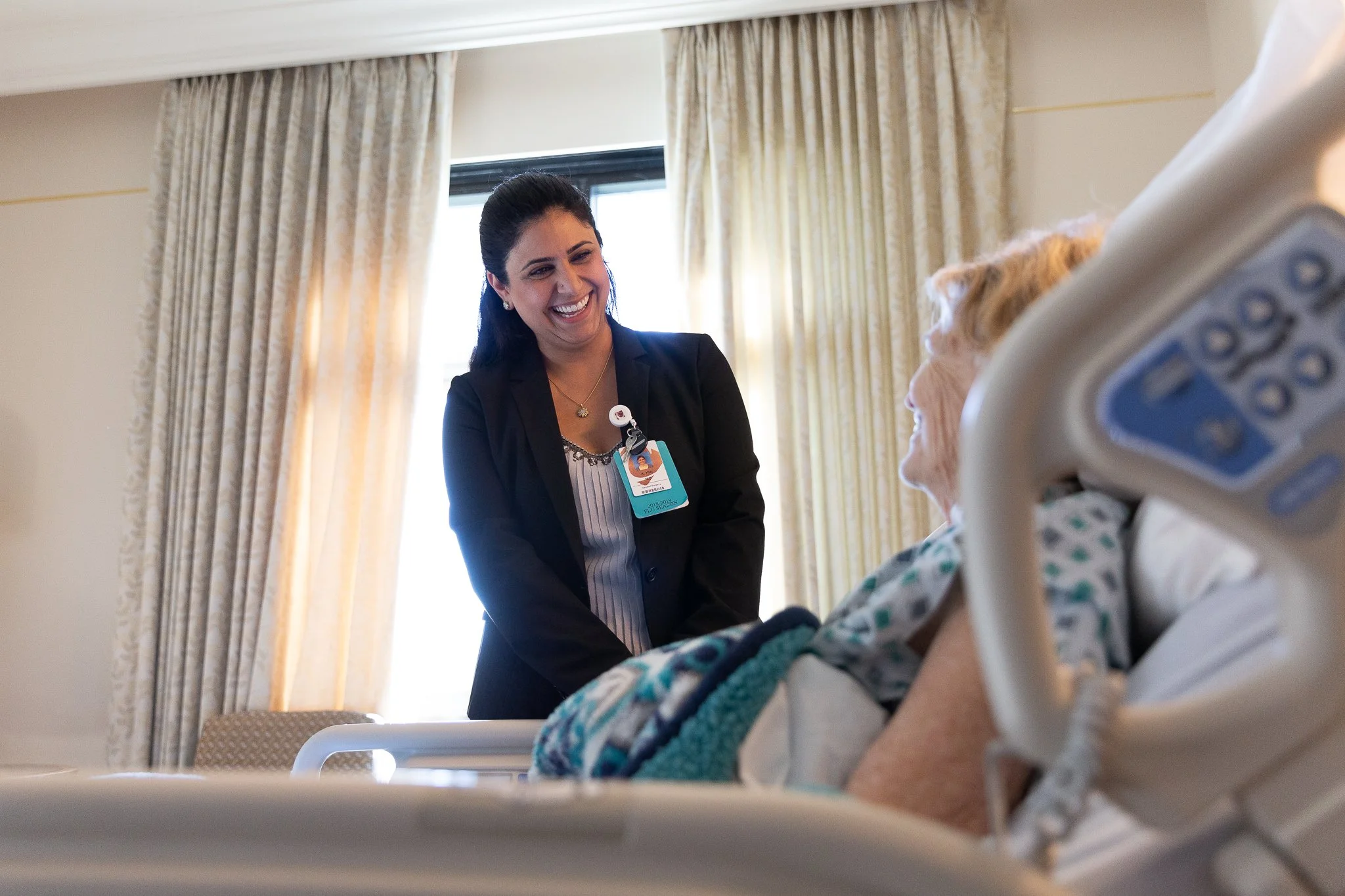 A young woman nurse is smiling and talking to an elderly patient lying in a hospital bed.