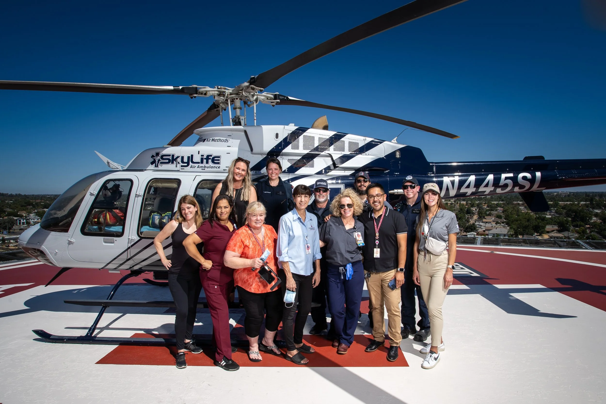 Group of healthcare professionals and staff standing in front of a SkyLife air ambulance helicopter on a helipad on a clear day.