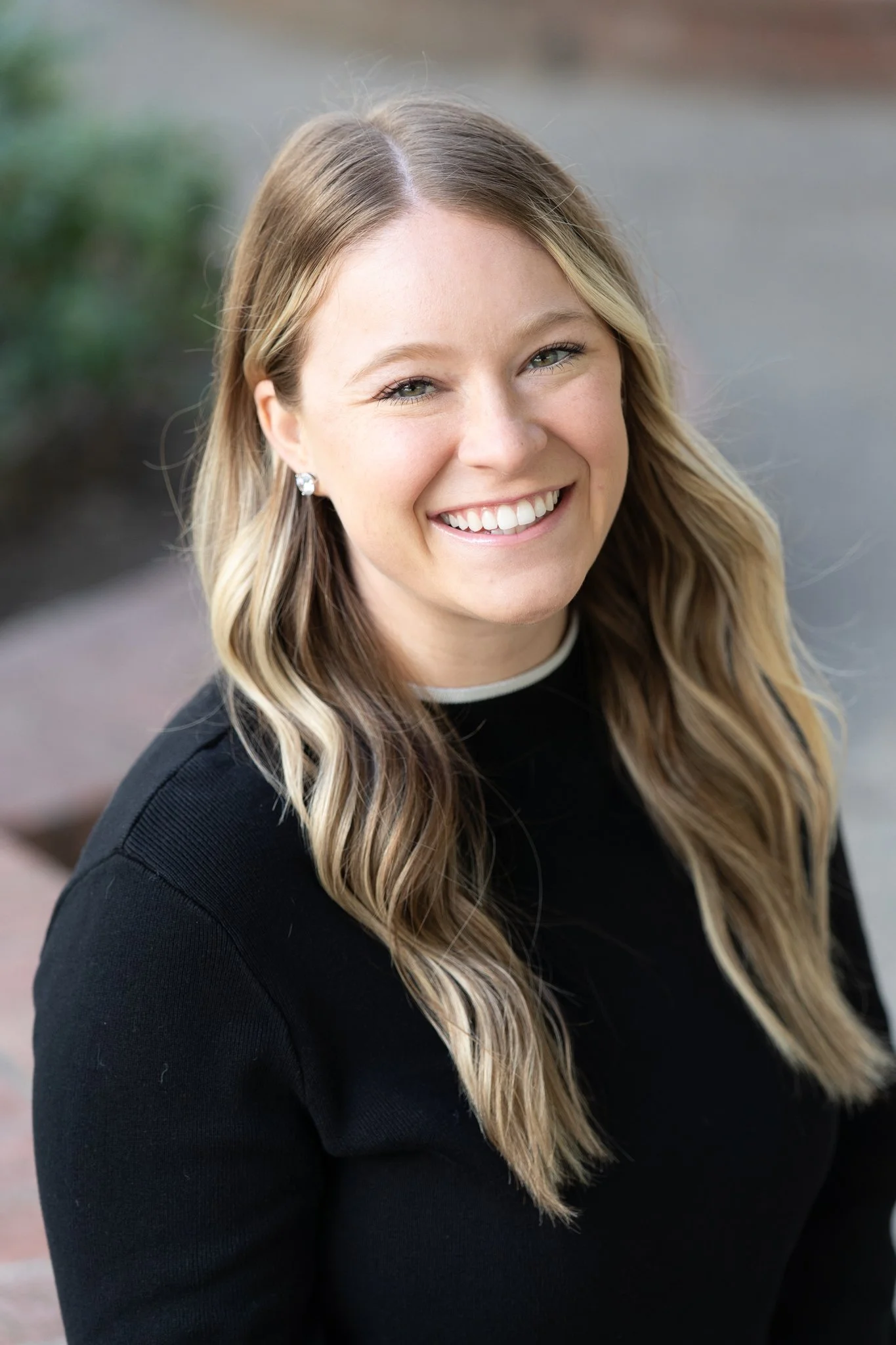 Young woman with wavy, blonde hair and earrings smiling outdoors.