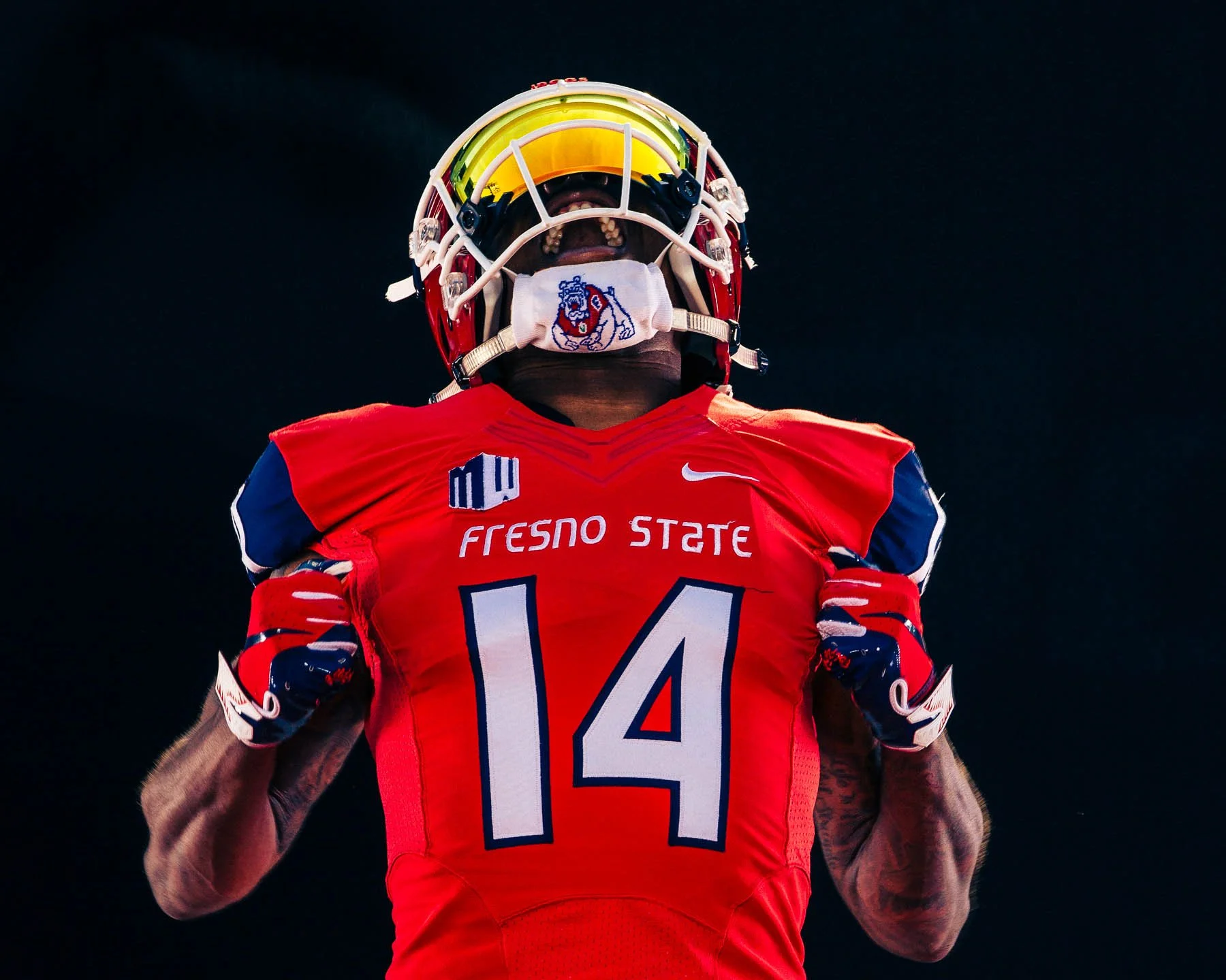 Fresno State football player wearing number 14 jersey, helmet with visor, and celebrating against a dark background.