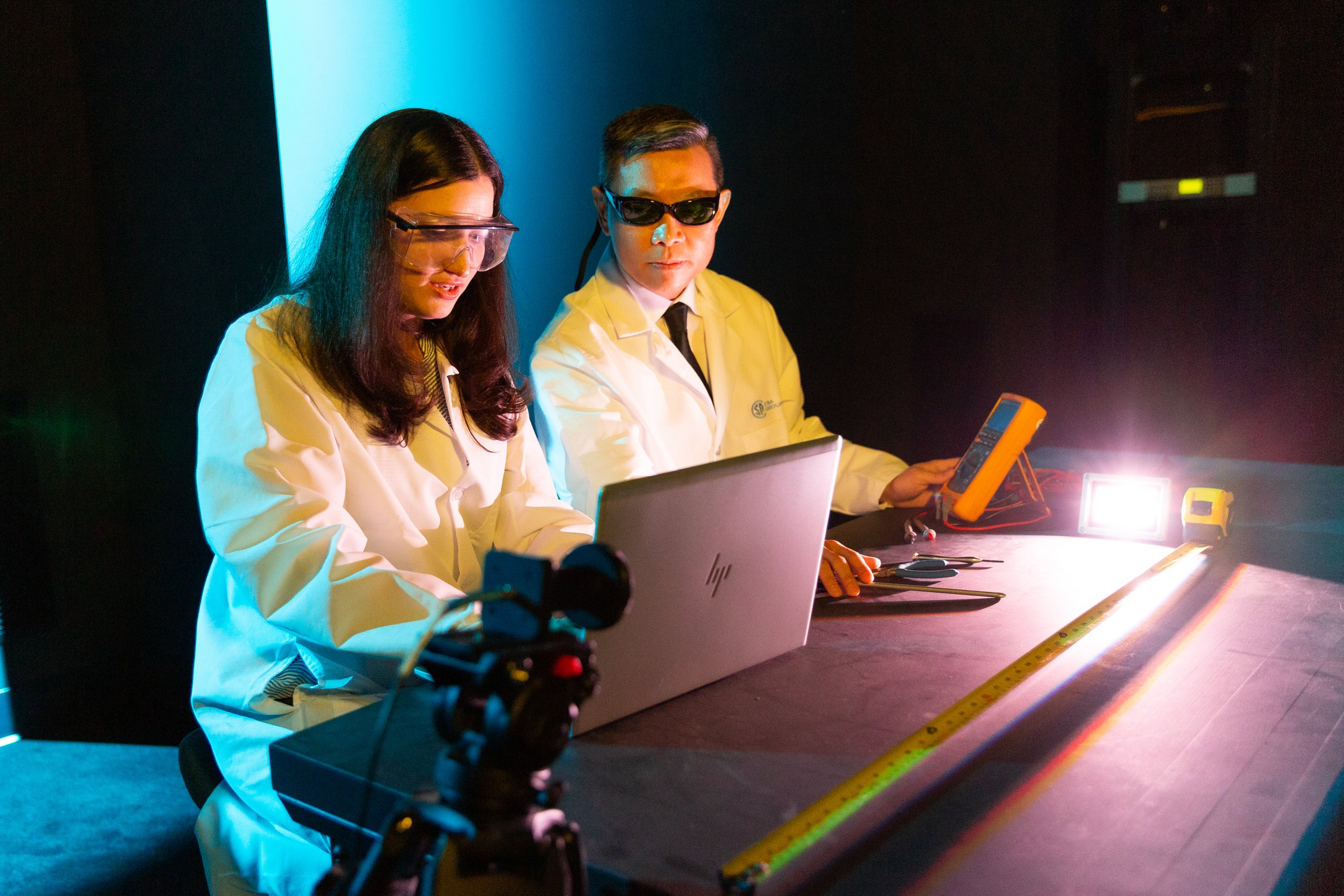 Scientists in white lab coats working with scientific equipment in a laboratory, illuminated by colorful lighting.