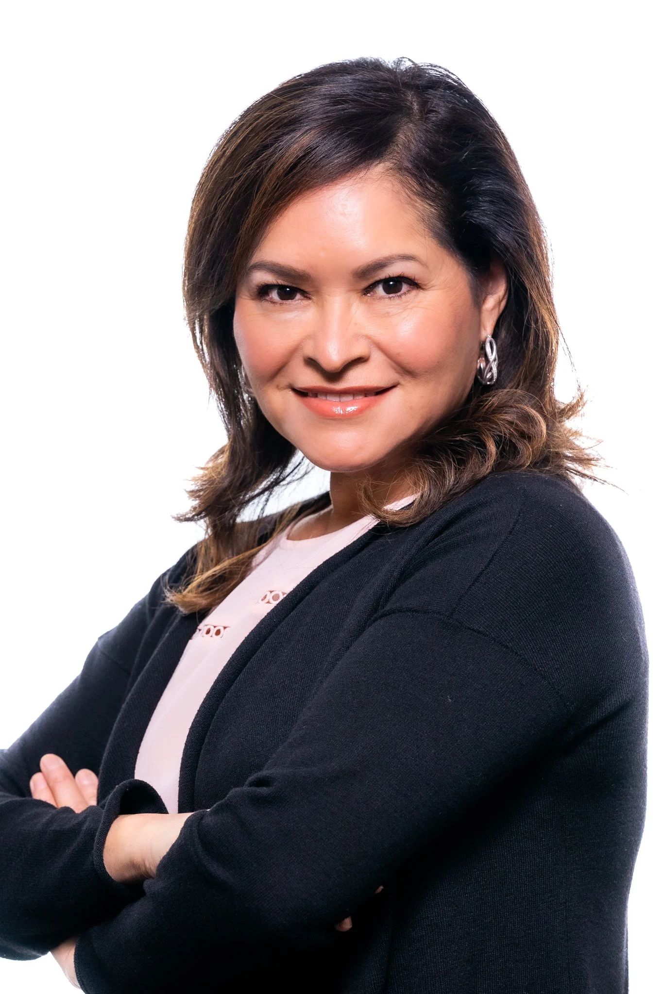 A woman with shoulder-length brown hair smiling, wearing a black blazer and a light-colored blouse, with her arms crossed.