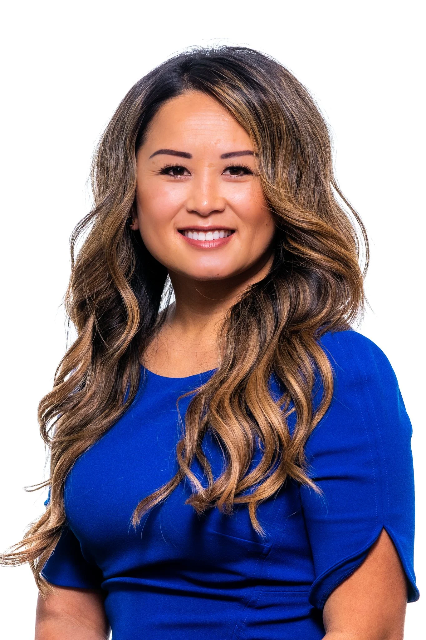A woman with long wavy brown hair, wearing a blue top, smiling against a plain white background.