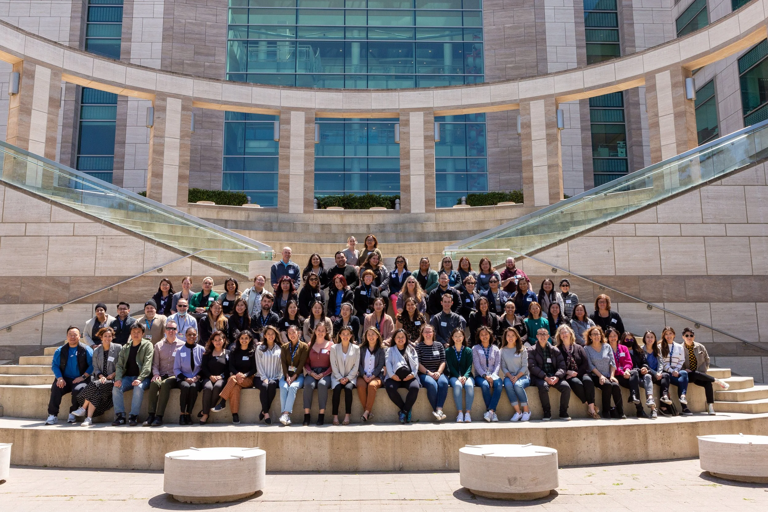 Group of people sitting and standing on steps outside modern building with large glass windows and staircases.