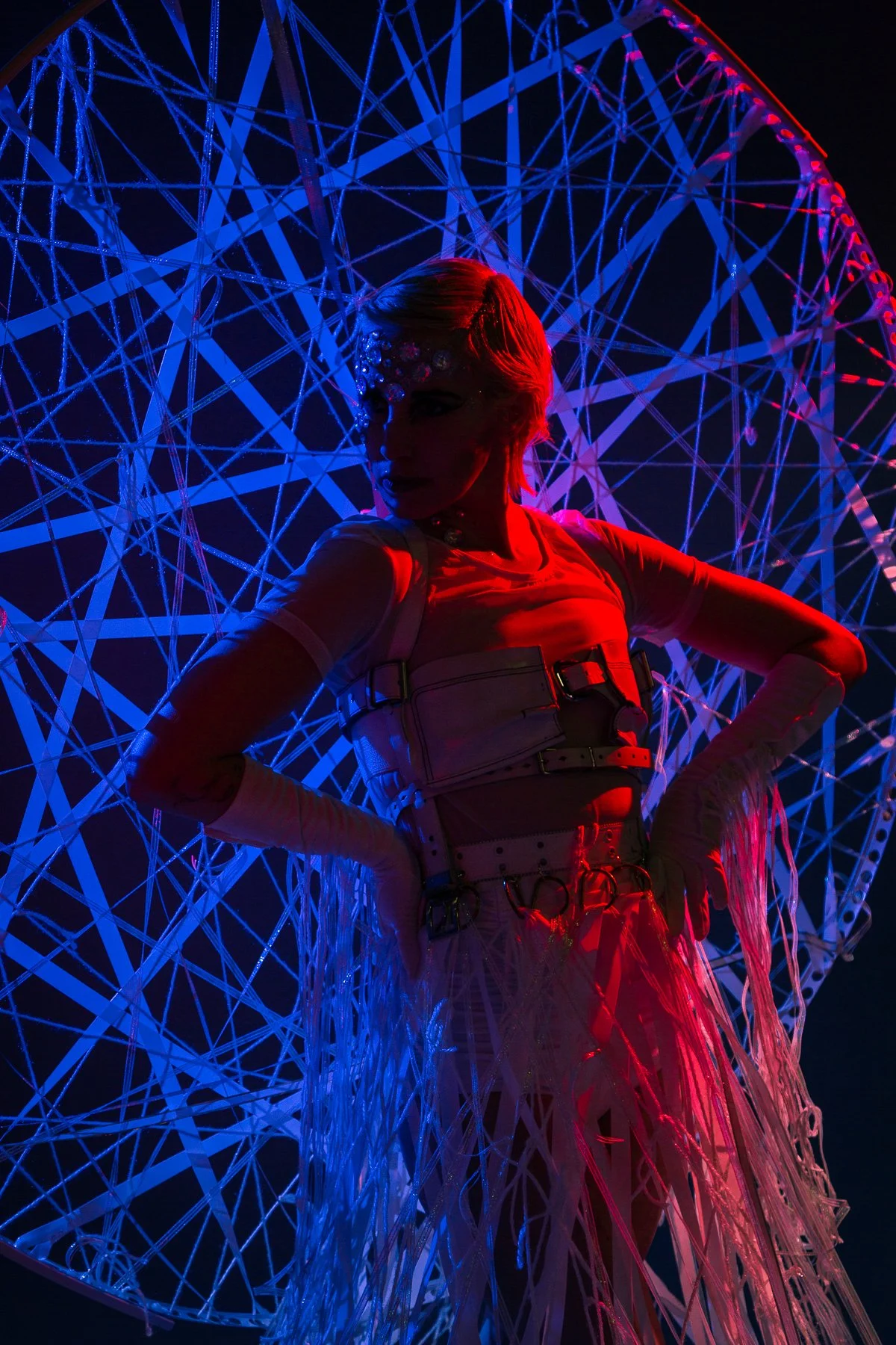 Person in futuristic outfit with geometric background illuminated by blue and red lights.