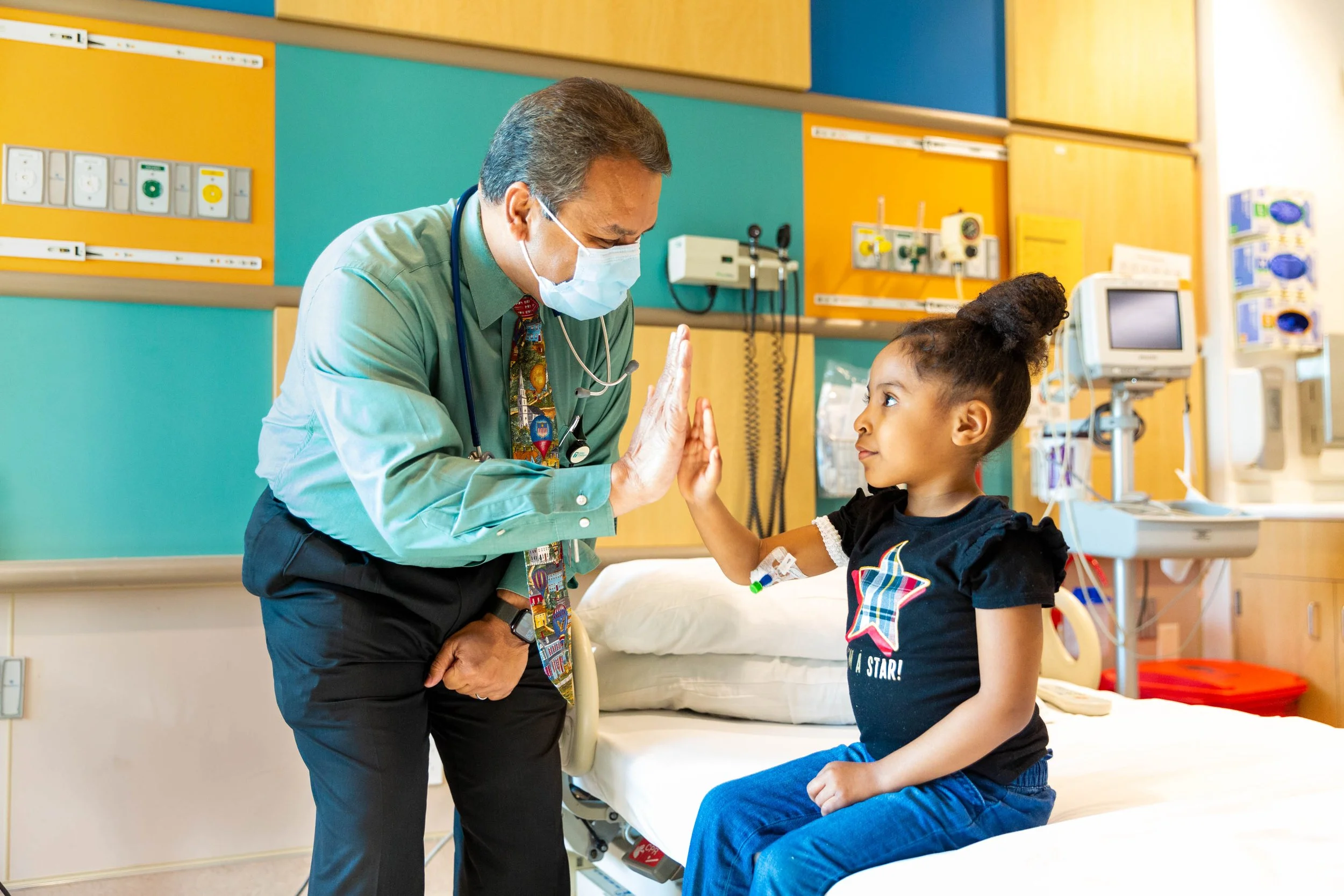 A doctor and a young girl in a hospital room giving each other a high five.