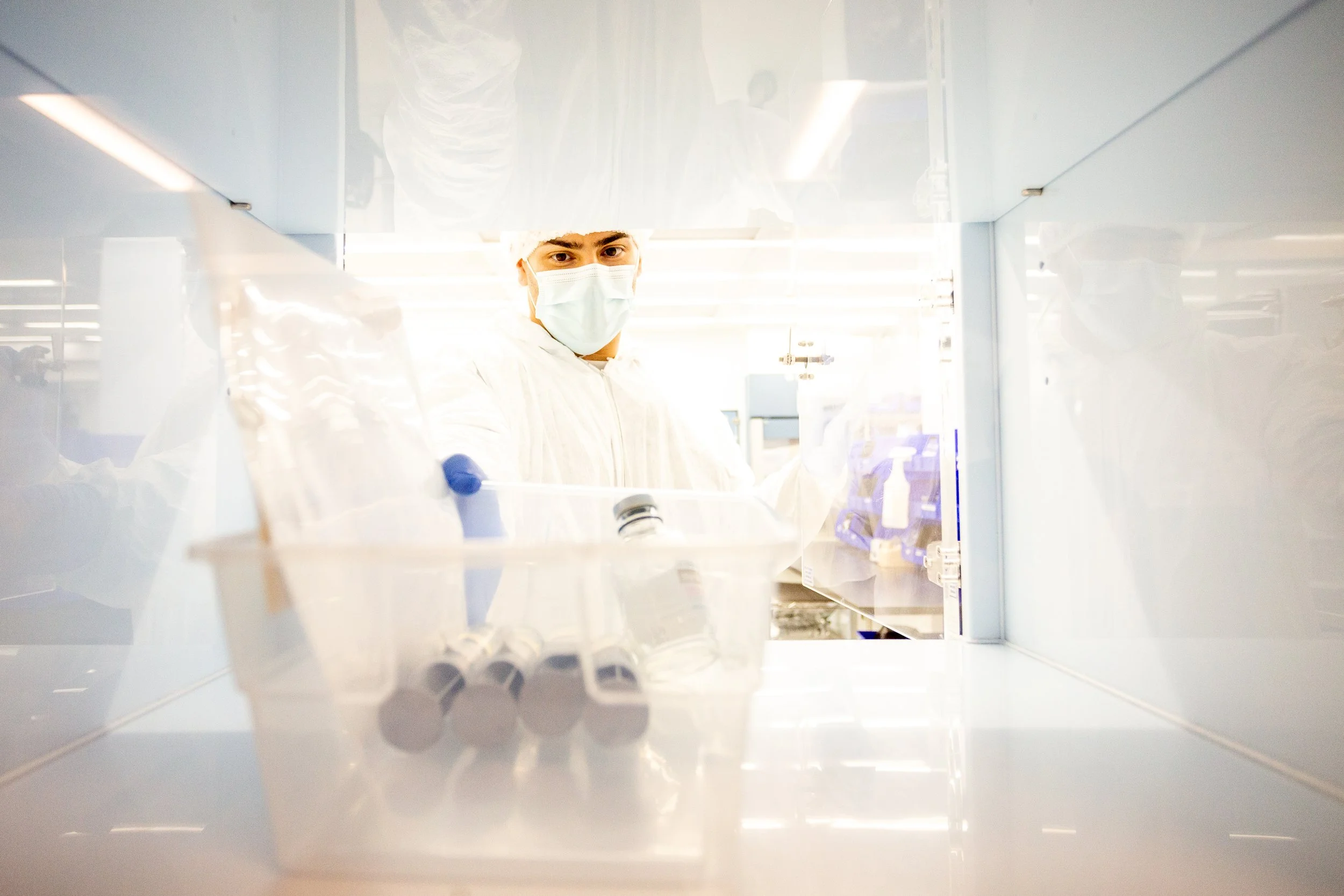 A scientist in protective clothing and face mask working in a laboratory with test tubes and lab equipment.