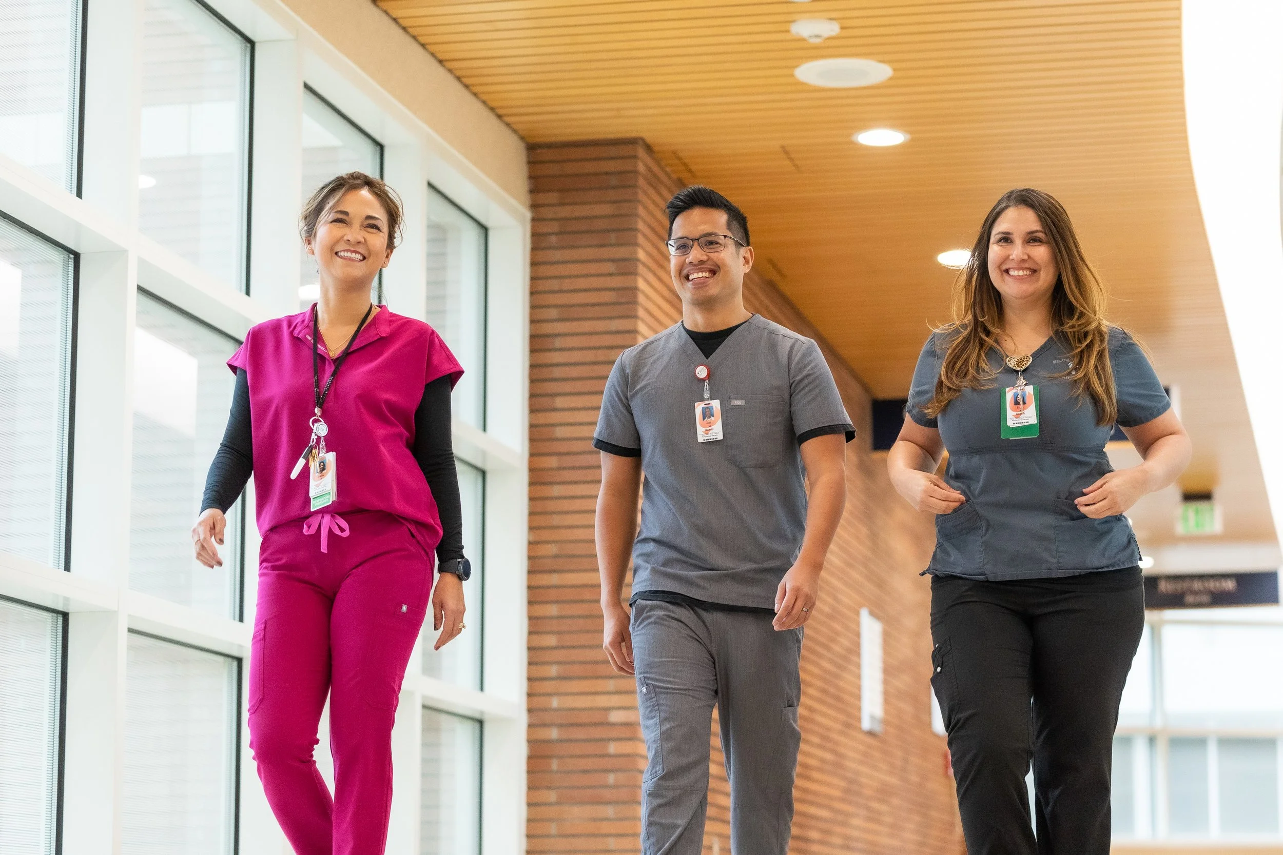 Three healthcare professionals walking and smiling in a hospital corridor.