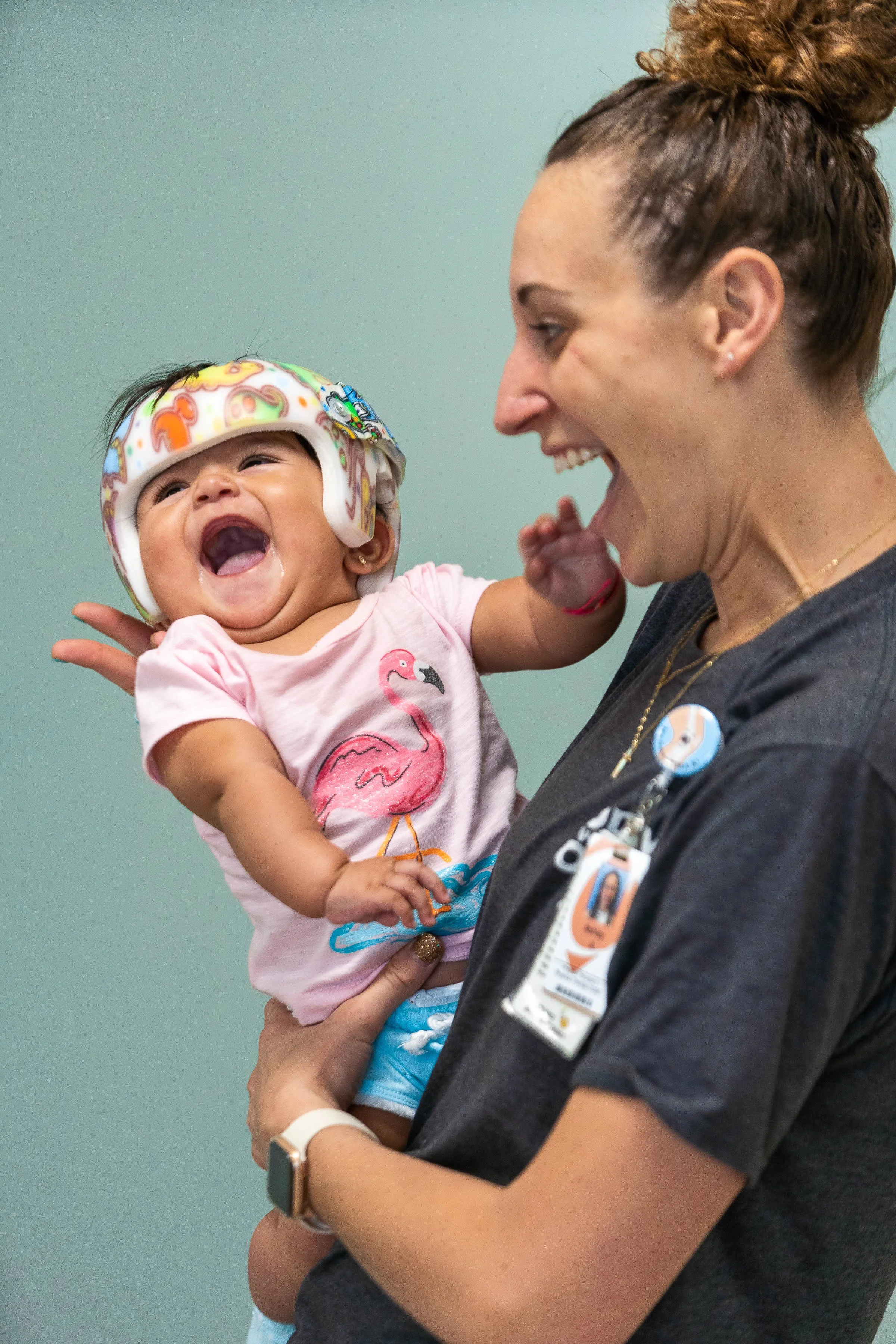 A nurse holding a laughing baby girl in a medical setting.