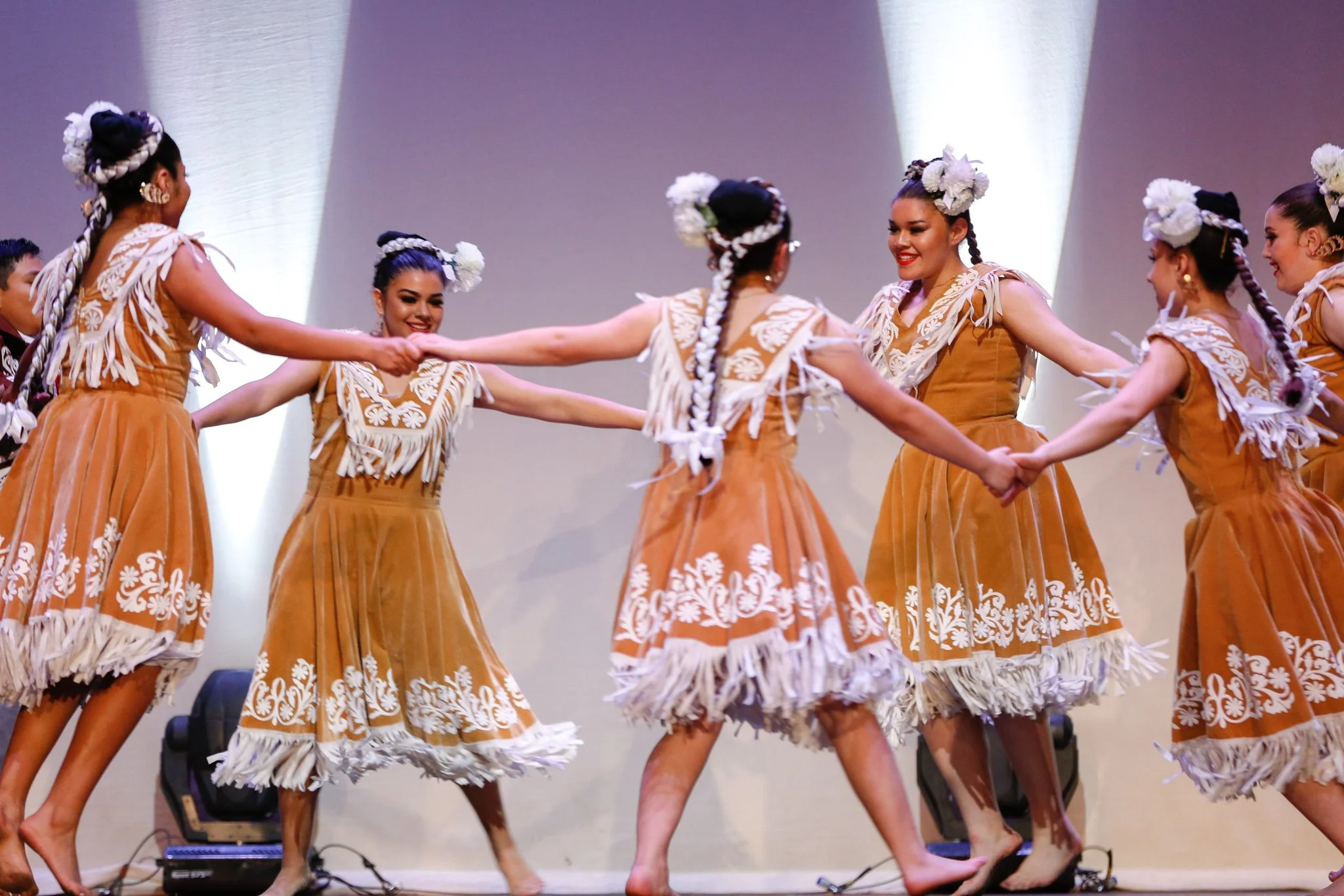 A group of women in traditional Polynesian costumes performing a hula dance on stage.