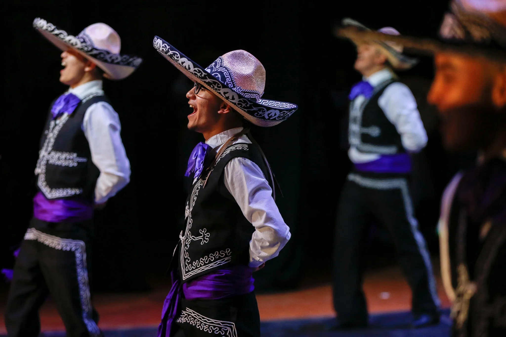 People wearing traditional Mexican Mariachi costumes with sombreros, standing on stage during a performance.