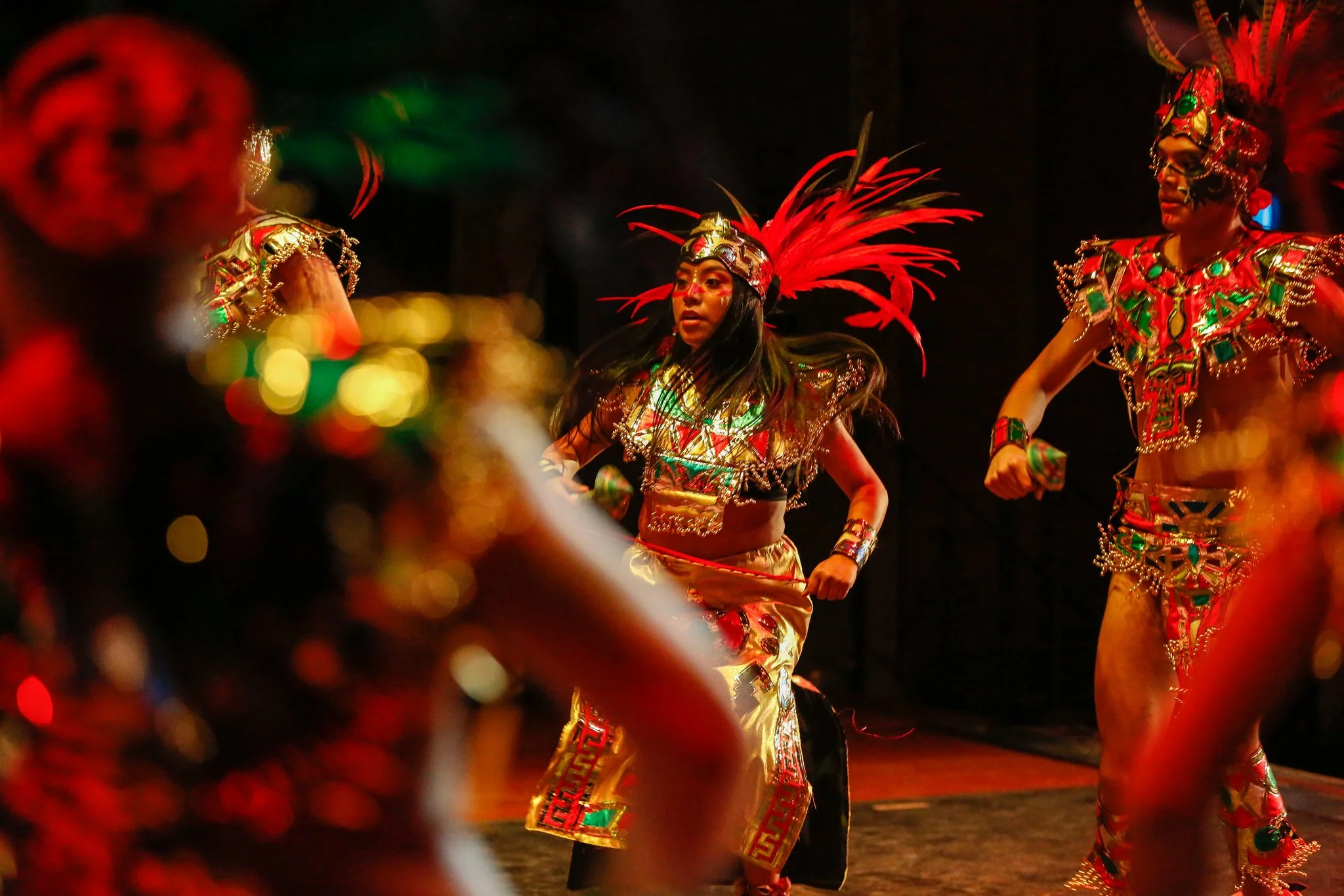 People dressed in vibrant traditional costumes with feathered headpieces, performing a dance on stage.