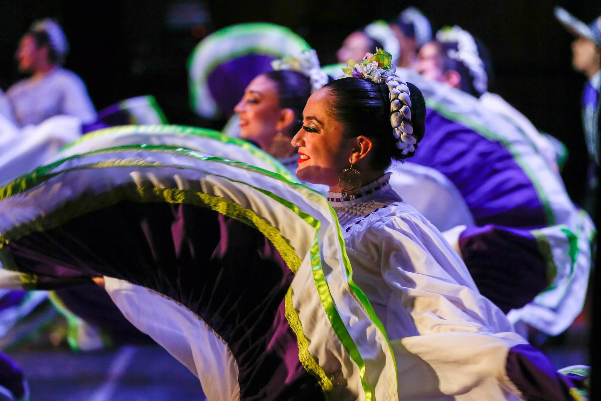 Women in traditional Mexican attire performing a dance with large fans.