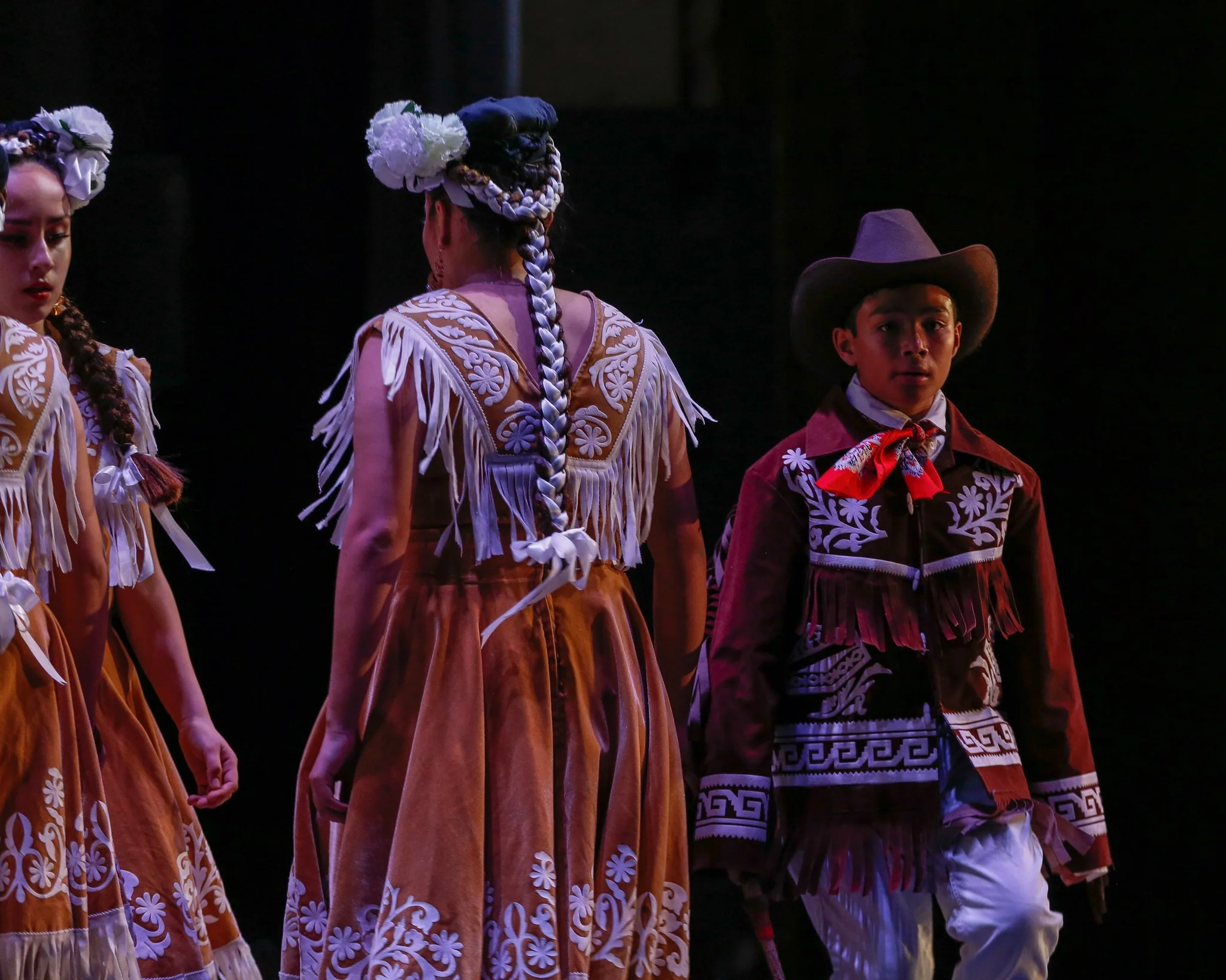 Children dressed in traditional Mexican folkloric costumes performing on stage.