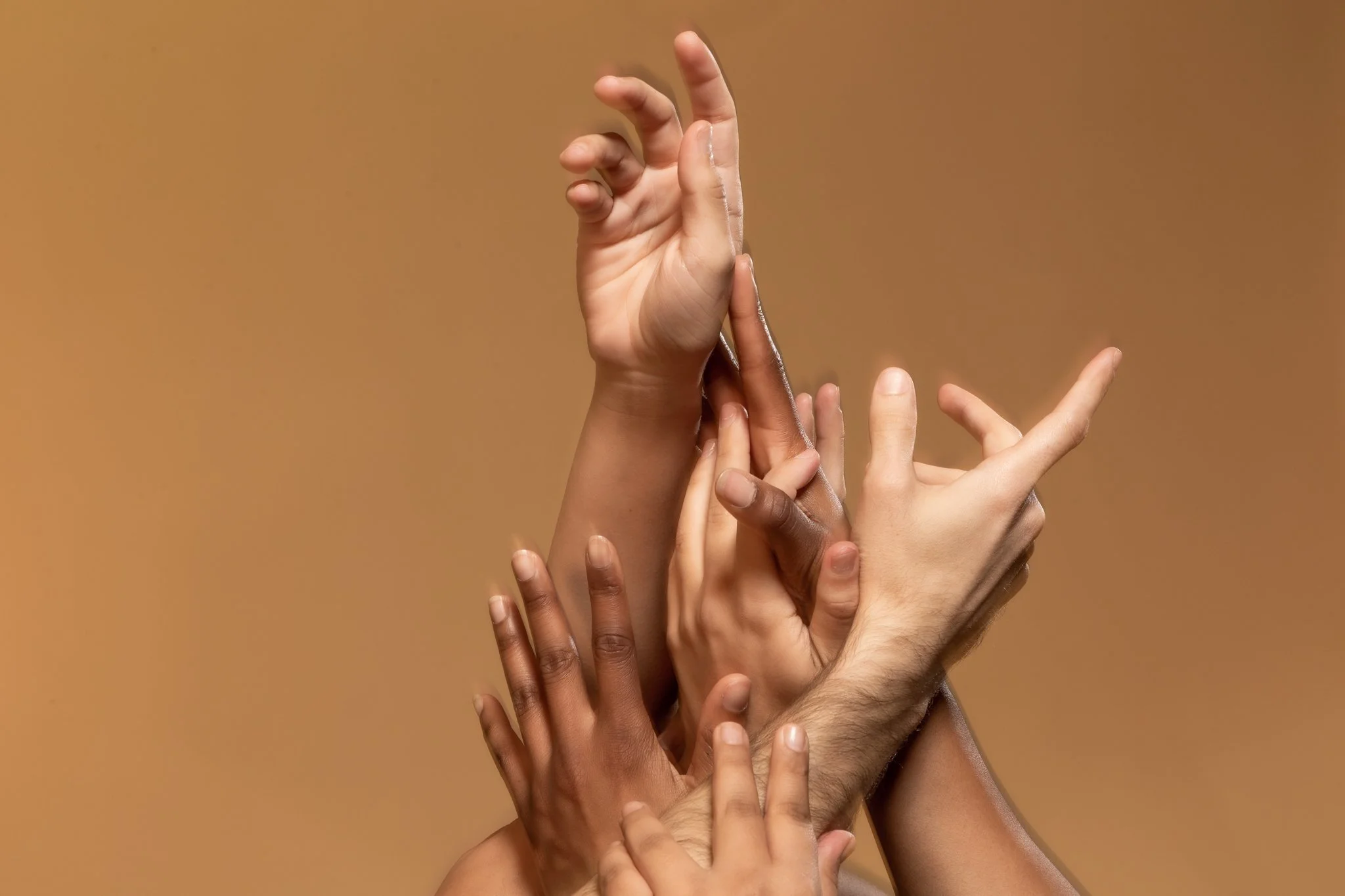 Multiple hands of different skin tones intertwining and reaching upward against a plain beige background.