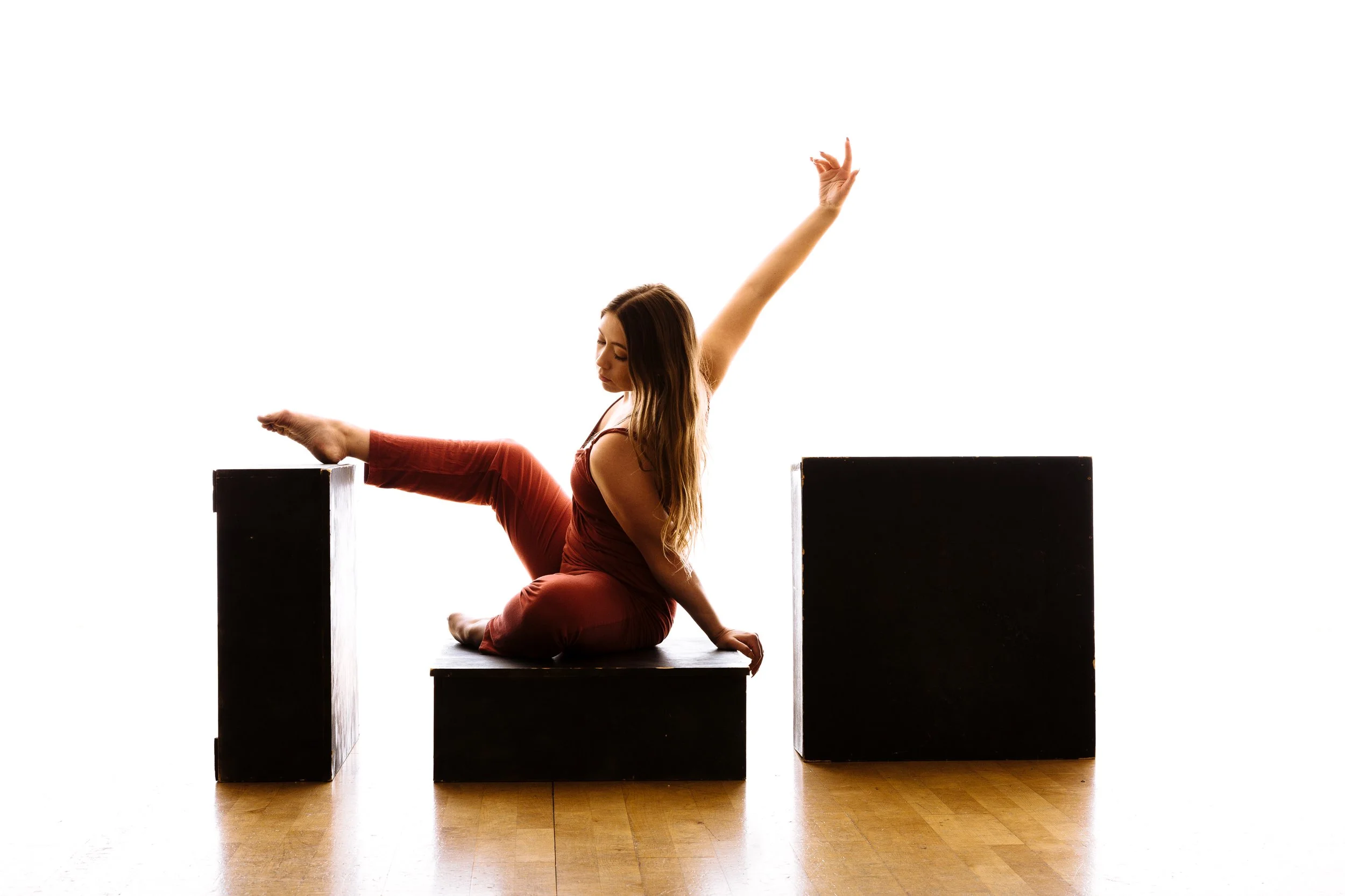 A woman performing a yoga pose on black blocks, with one leg extended and arm raised, against a white background.