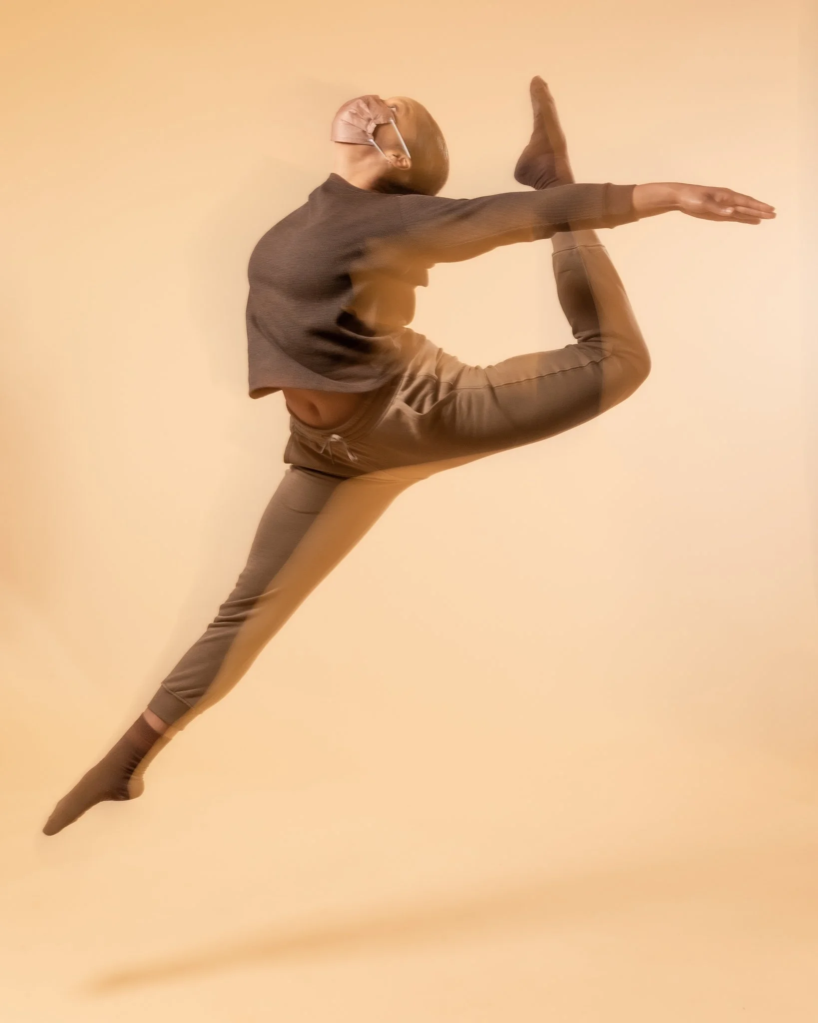 Person in motion stretching or performing a dance move against a beige background.