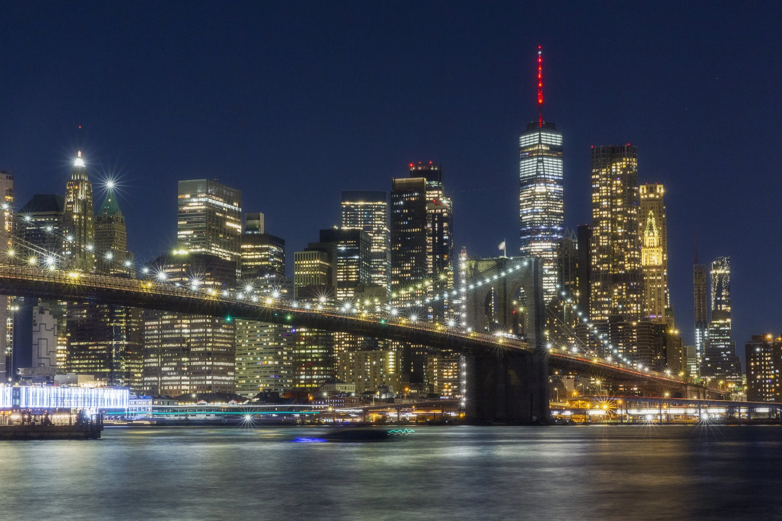 Night view of Brooklyn Bridge and Manhattan skyline with illuminated skyscrapers in New York City.