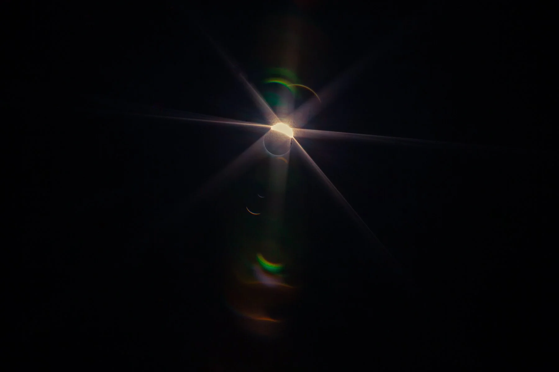 An image capturing a solar eclipse with the Moon covering part of the Sun, producing a bright corona with lens flare effects and rainbow-colored halos.