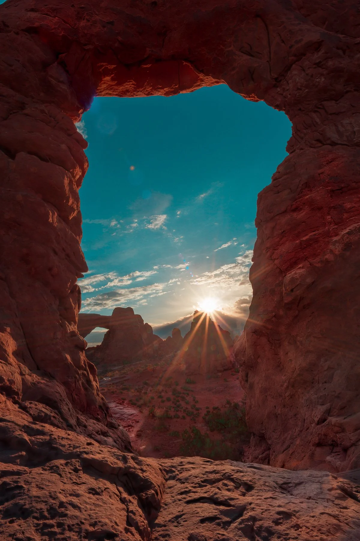 Sun rising over red rock formations in Arches National Park, viewed through a natural rock arch