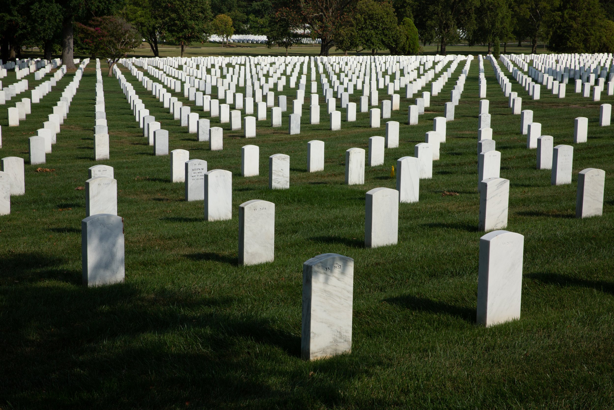 A large military cemetery with evenly spaced white marble headstones on green grass, trees in the background.
