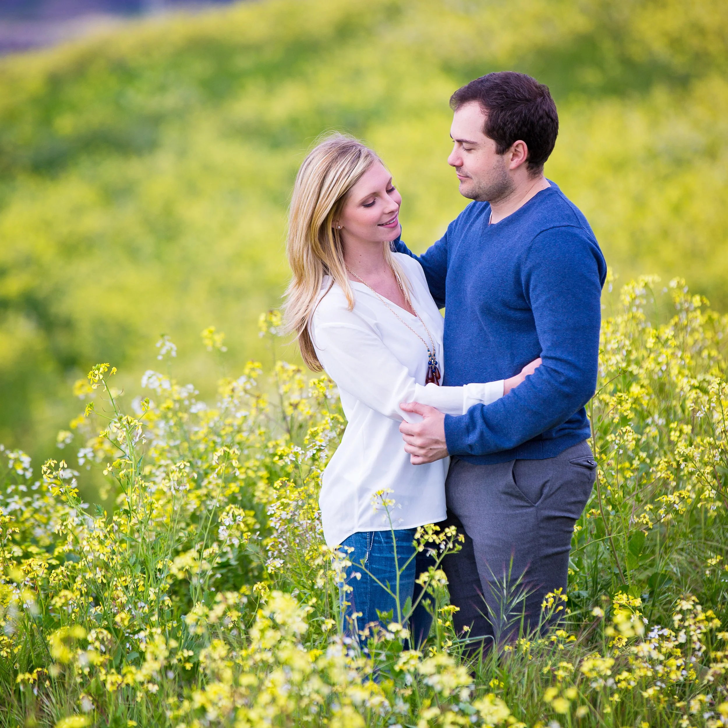 A couple hugging and smiling in a field of yellow flowers with a blurred green background.