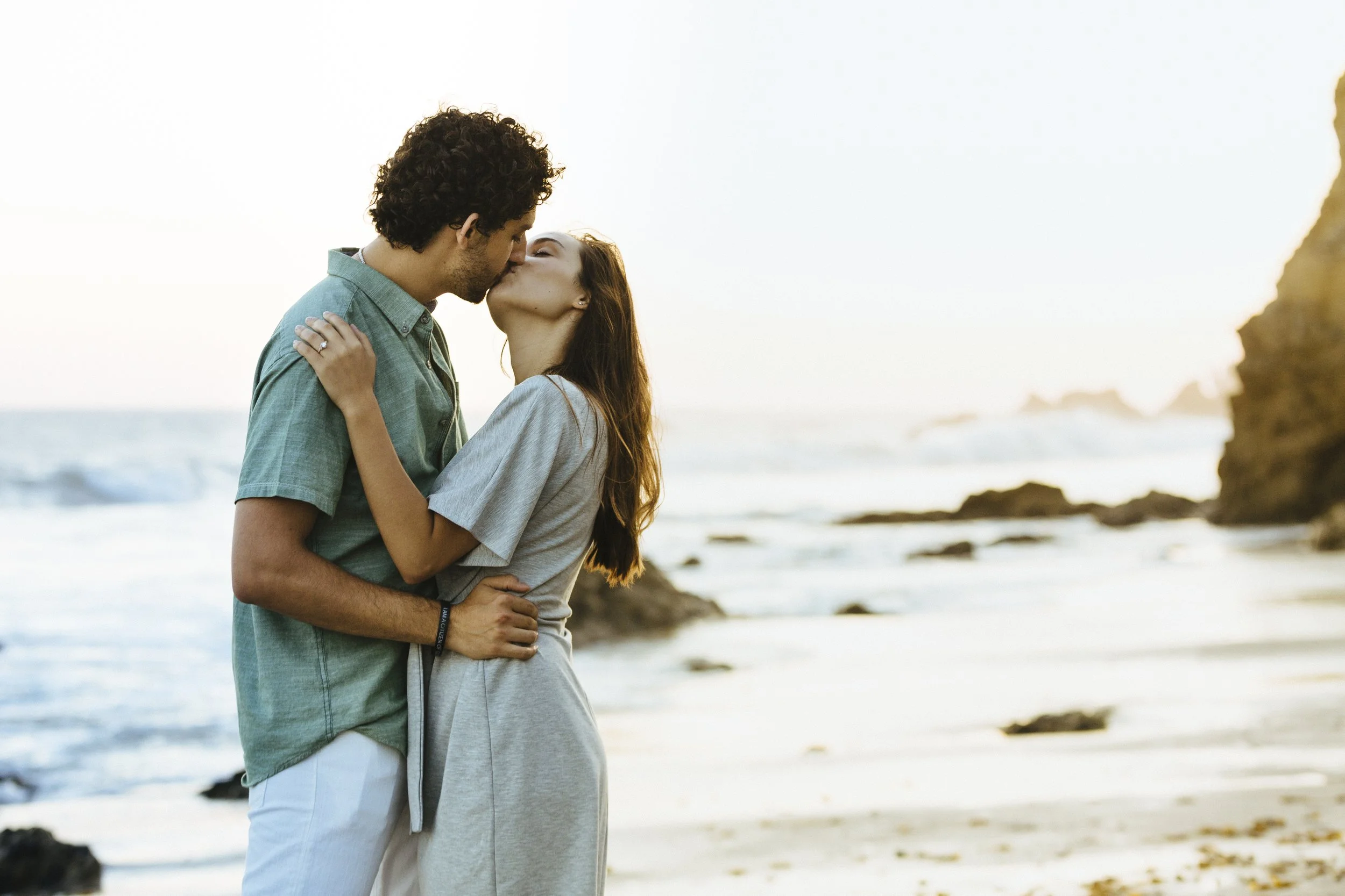 A young couple sharing a kiss on a beach during sunset.
