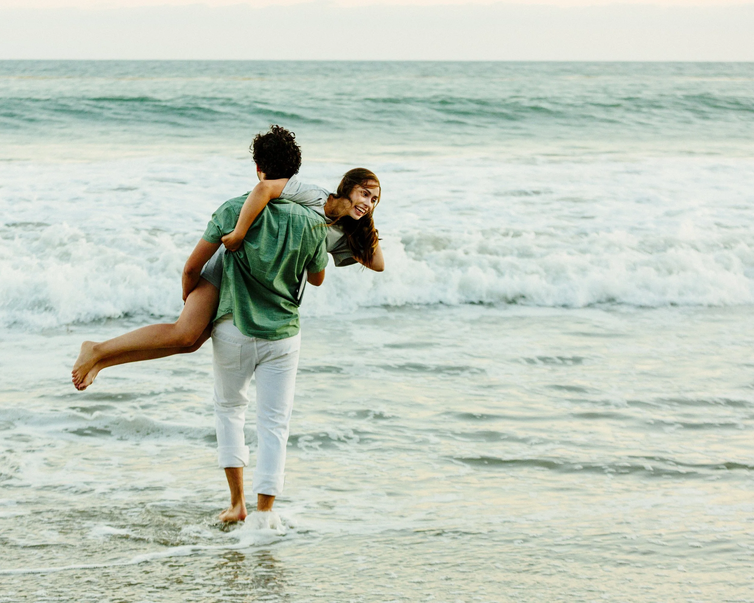 A man carrying a woman on the beach near the water