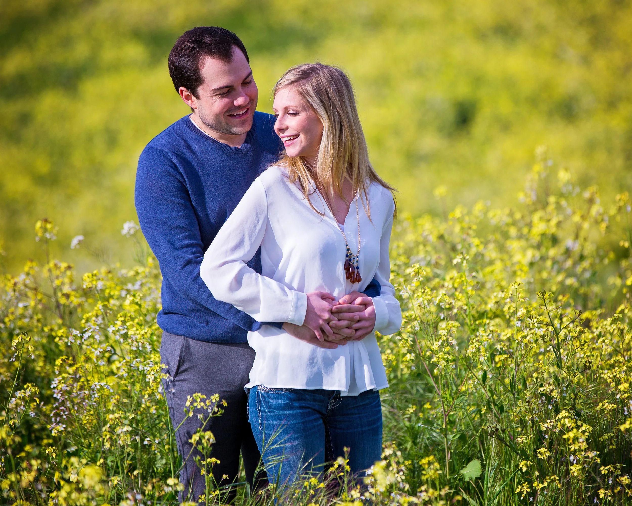 A happy couple embracing in a yellow flower field on a sunny day.