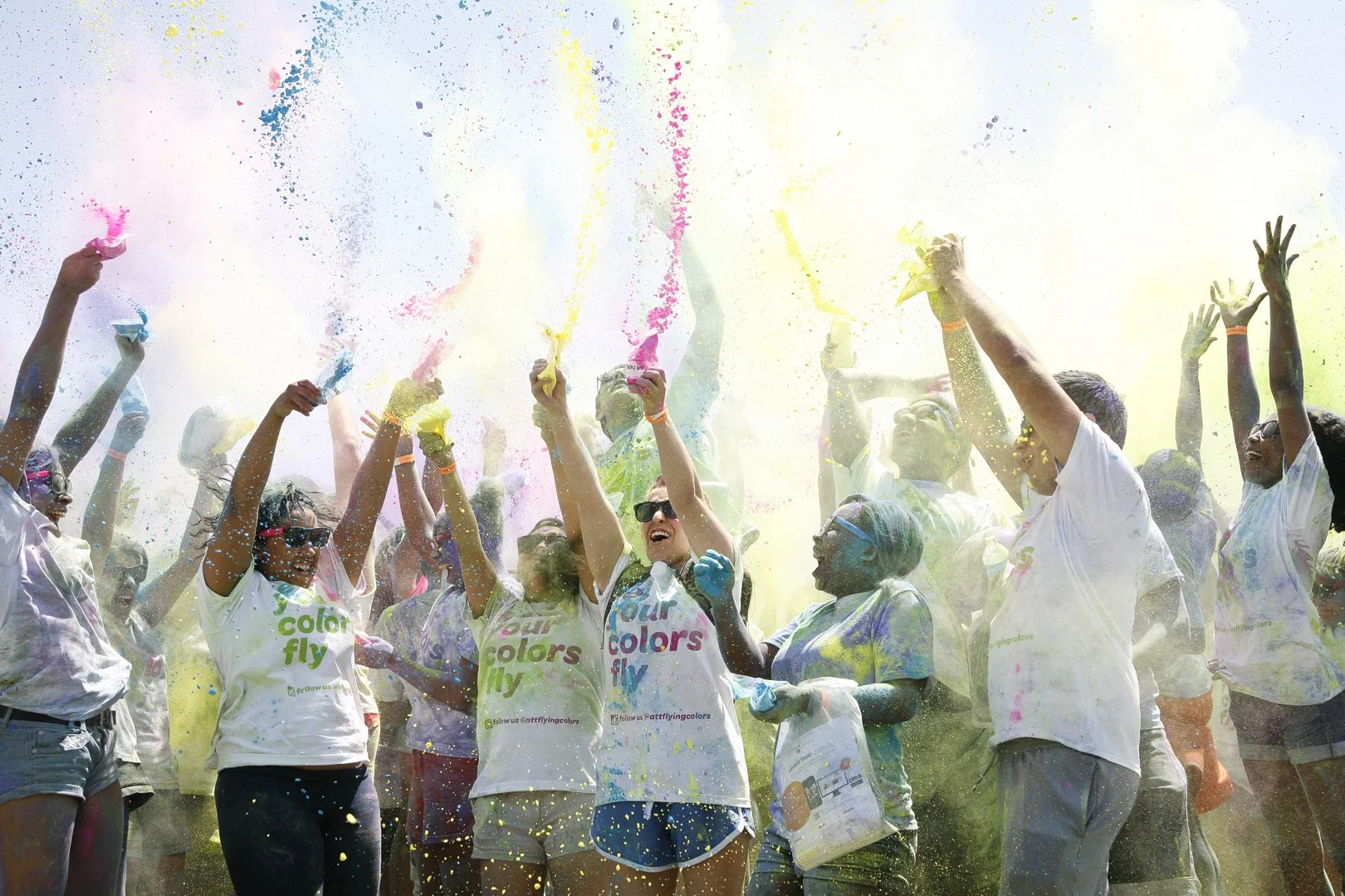 People celebrating at a color run event, throwing colored powder into the air and wearing white t-shirts.