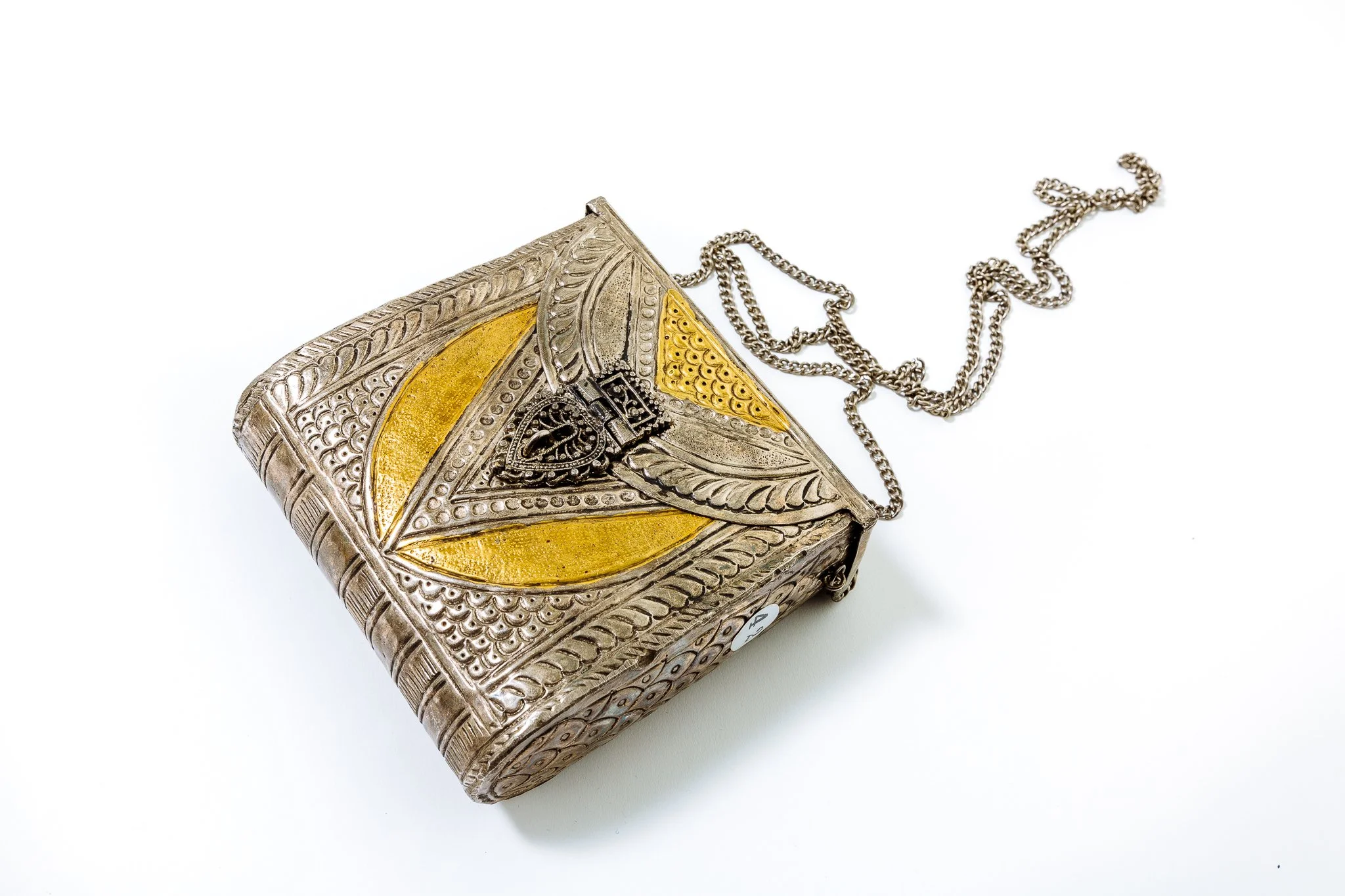 An ornate silver purse with gold accents and a silver chain strap, featuring intricate decorative patterns.