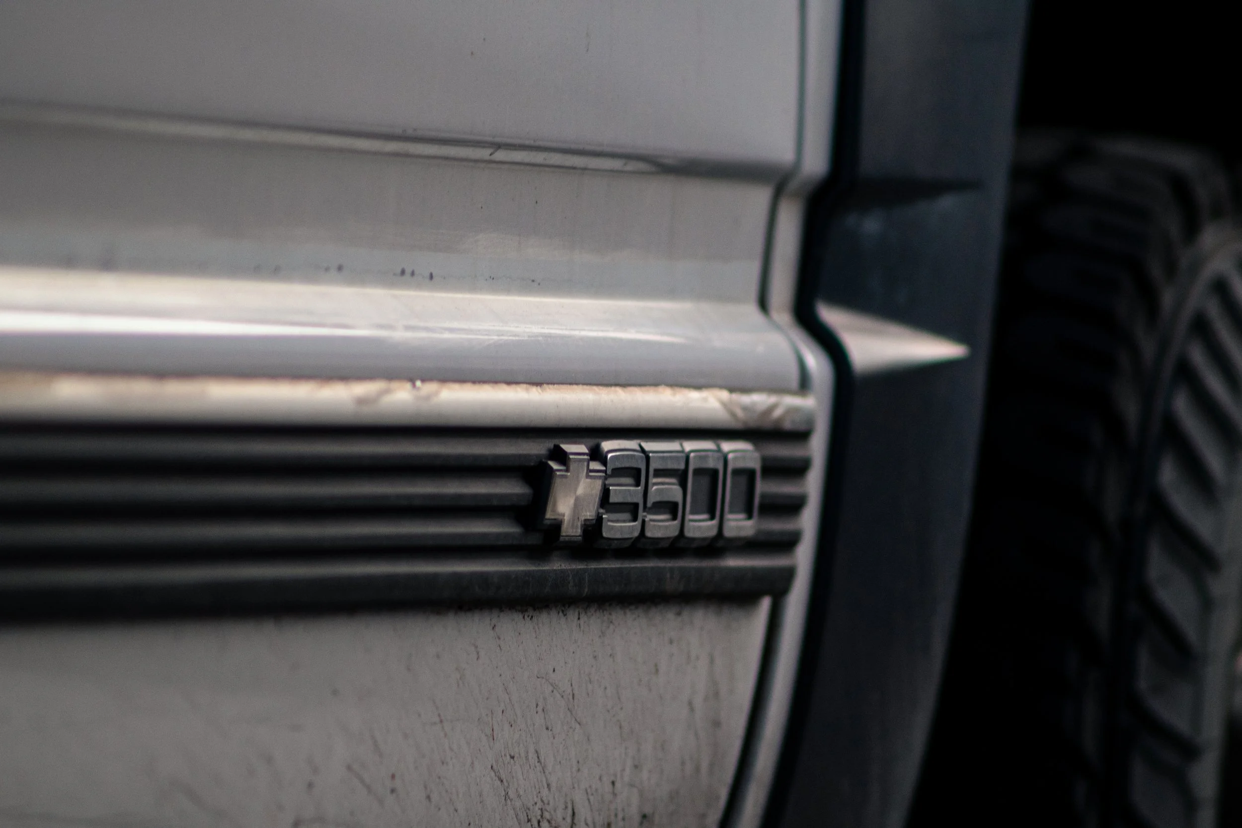 Close-up of a silver Chevrolet 3500 emblem on a black vehicle, showing part of the grille and bumper.