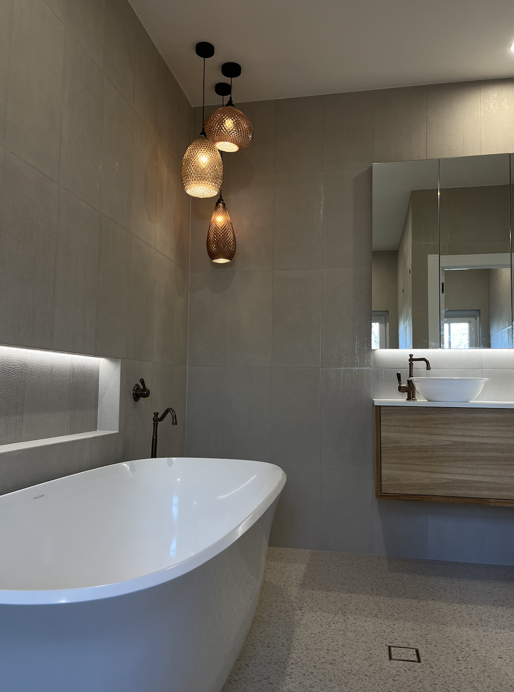 Modern bathroom with freestanding bathtub, wood vanity with vessel sink, large mirror, and decorative pendant lights.
