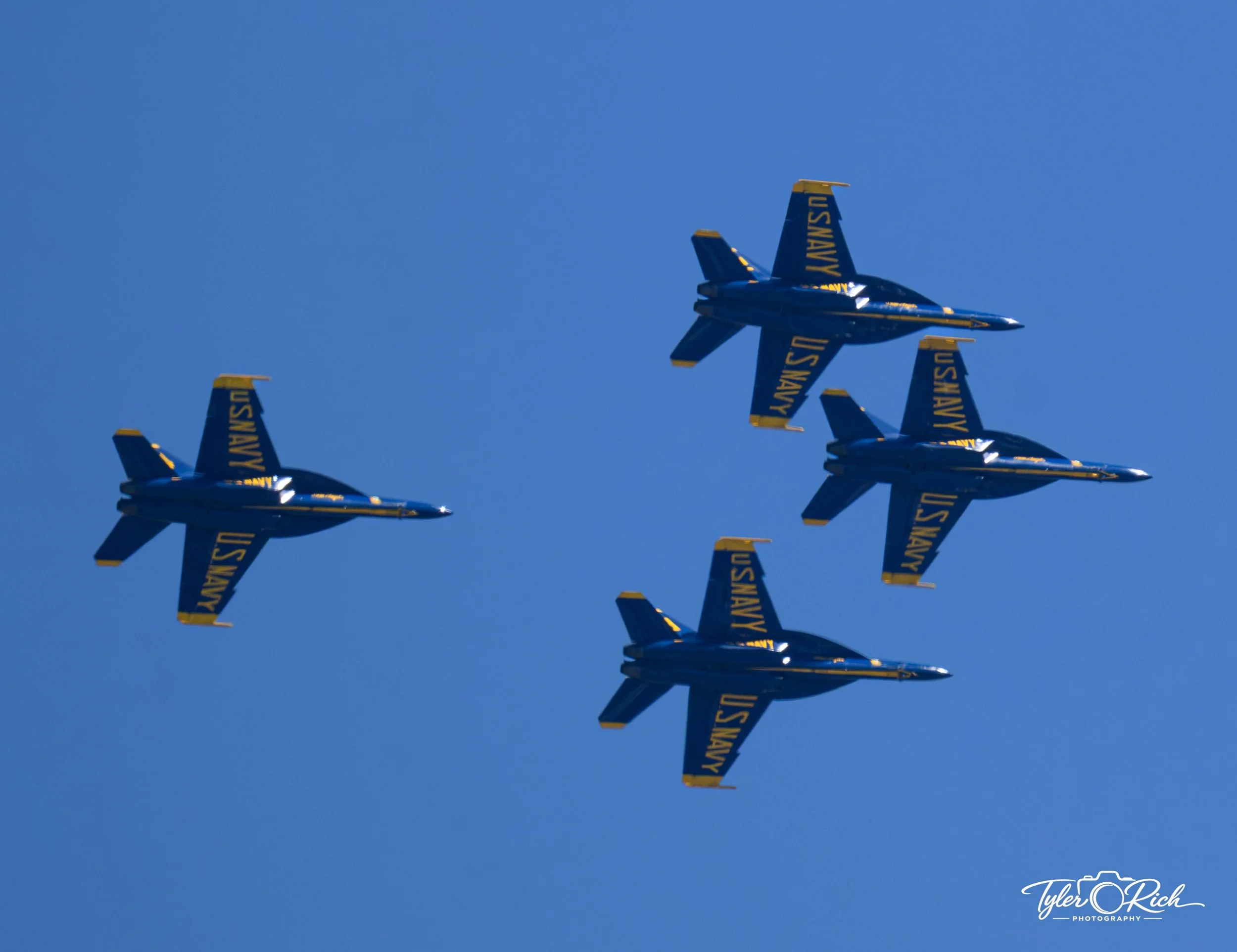 Three US Navy fighter jets flying in formation against a clear blue sky.