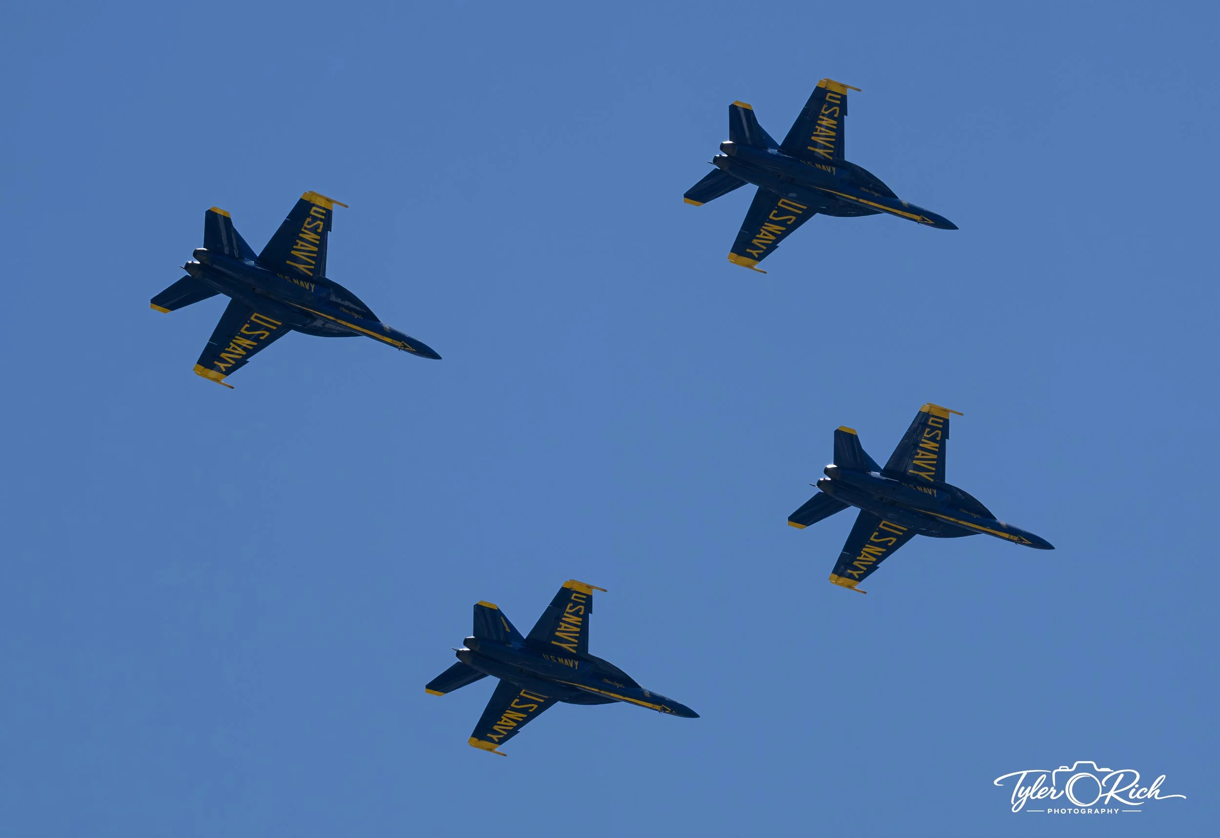 Four U.S. Navy Blue Angels fighter jets flying in a diagonal formation against a clear blue sky.