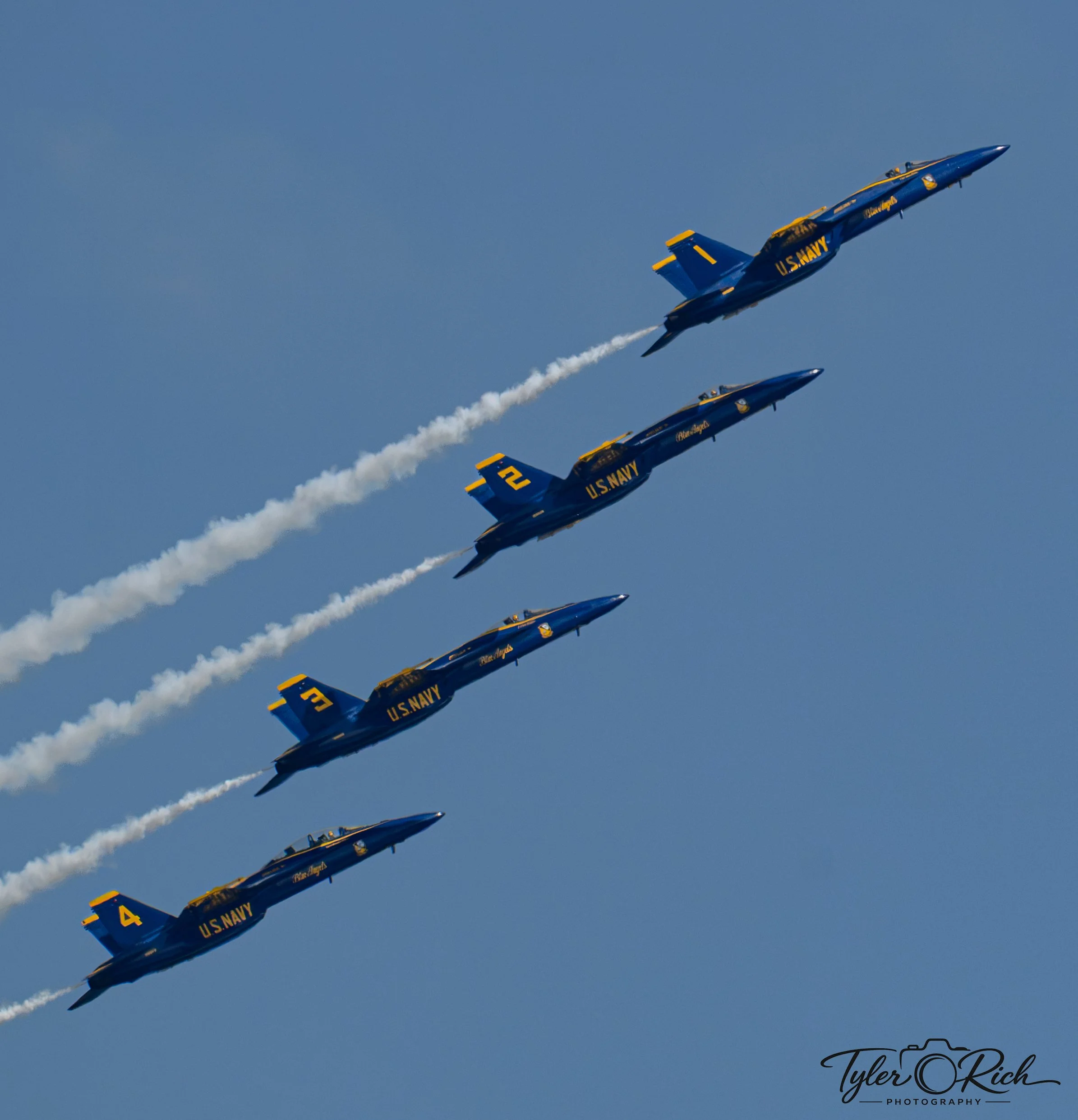 Blue U.S. Navy fighter jets flying in tight formation in the sky, leaving white smoke trails behind them.