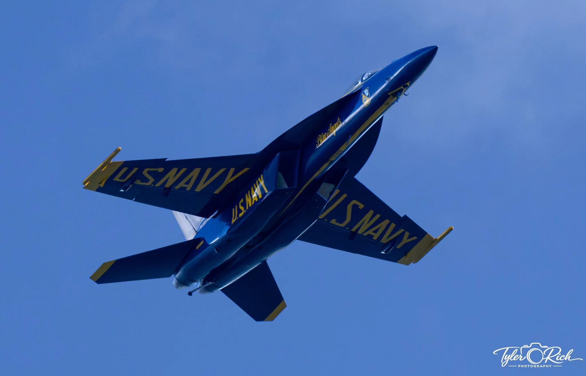 A U.S. Navy fighter jet flying in a clear blue sky.