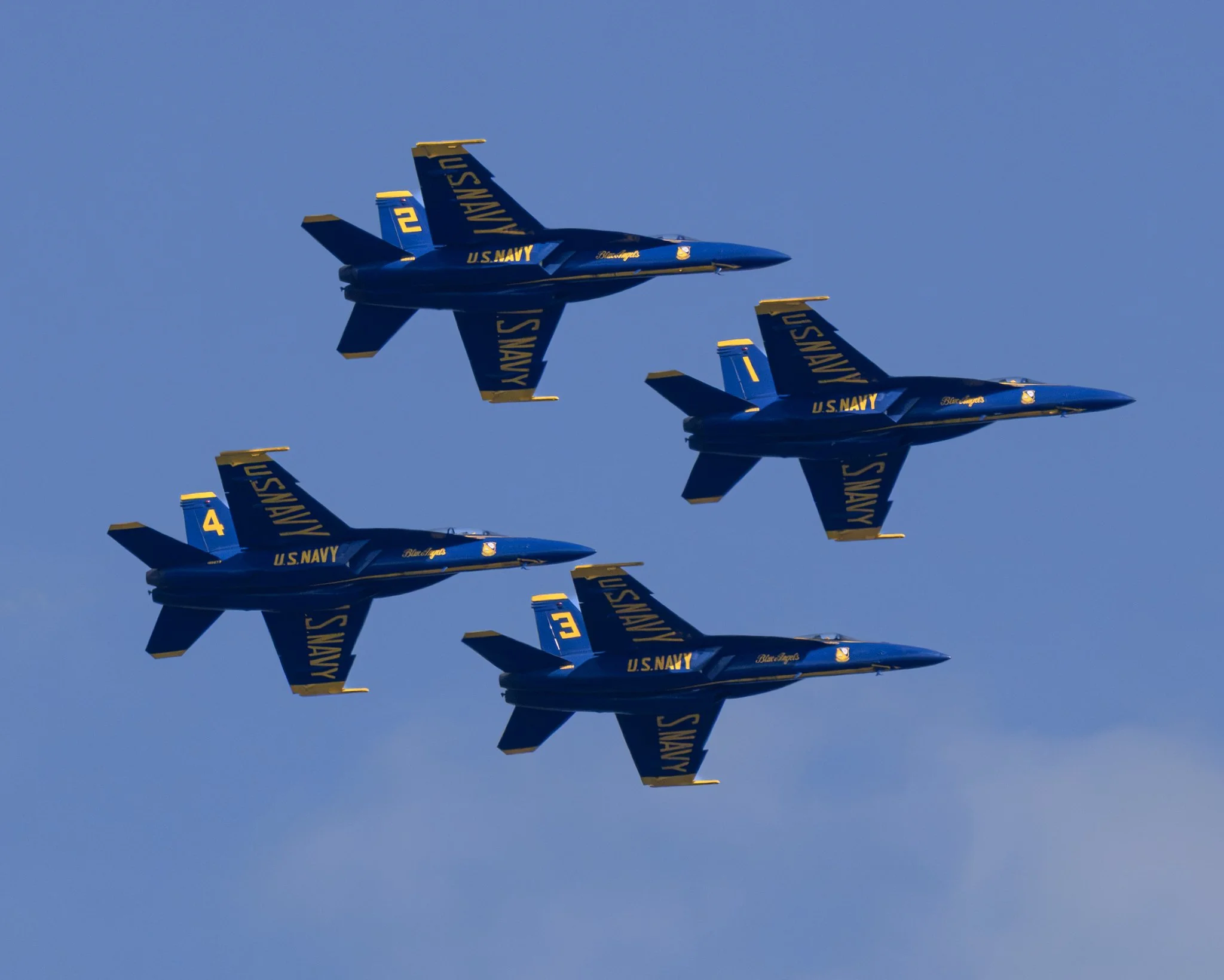 Three US Navy Blue Angels fighter jets flying in a tight formation against a clear blue sky.