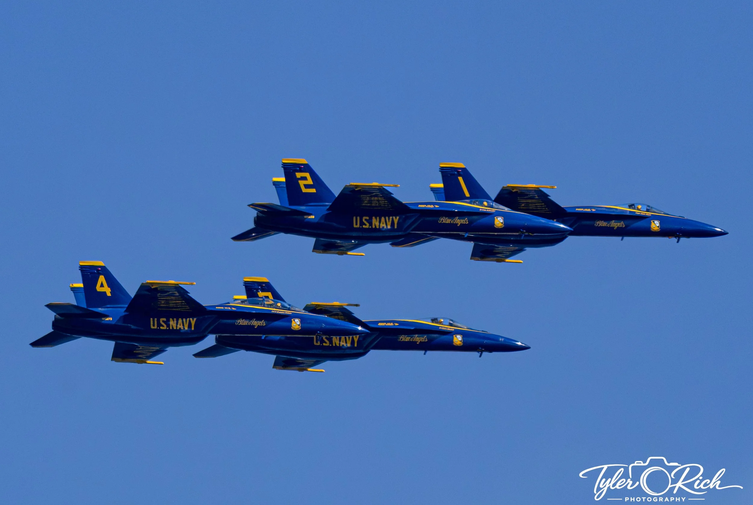 Blue U.S. Navy Blue Angels fighter jets flying in close formation against a clear blue sky.