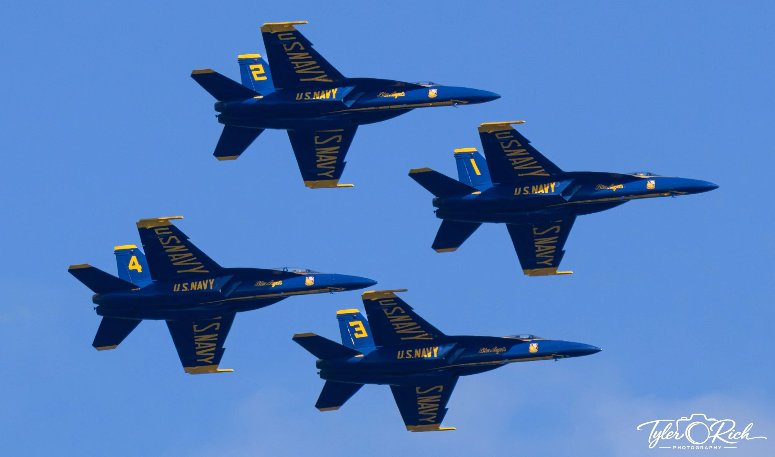 Blue U.S. Navy jets flying in close formation against a clear blue sky.